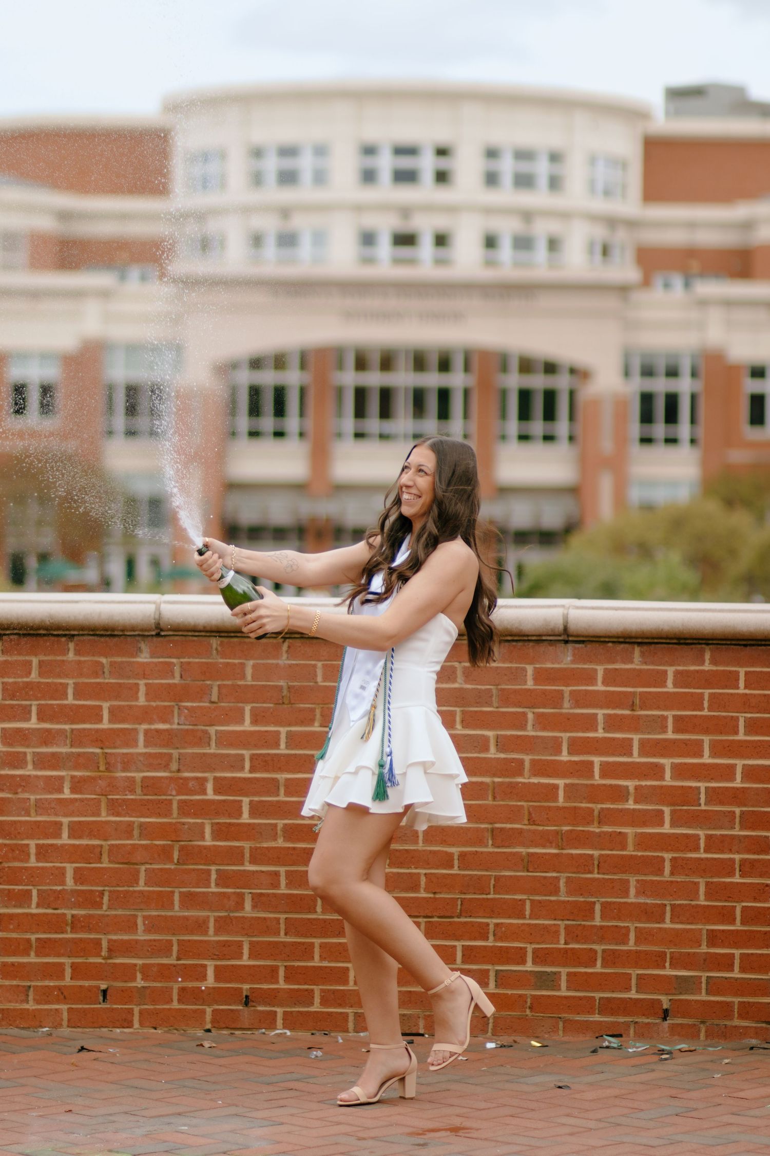 A person in white sits on a brick wall with a university building in the background.