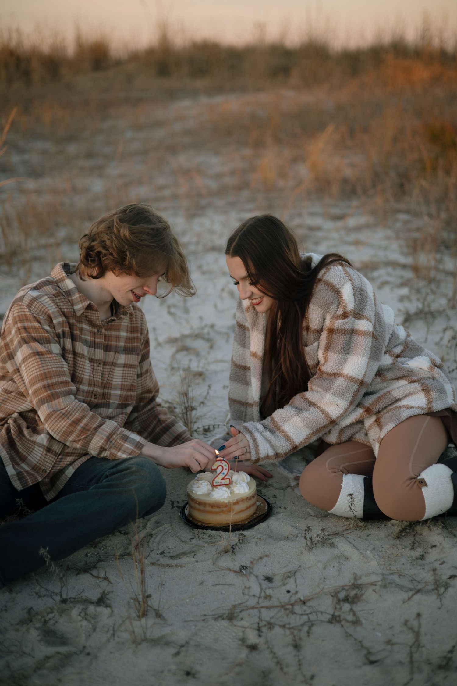 A couple shares sweet moments while sitting on sandy ground during golden hour.
