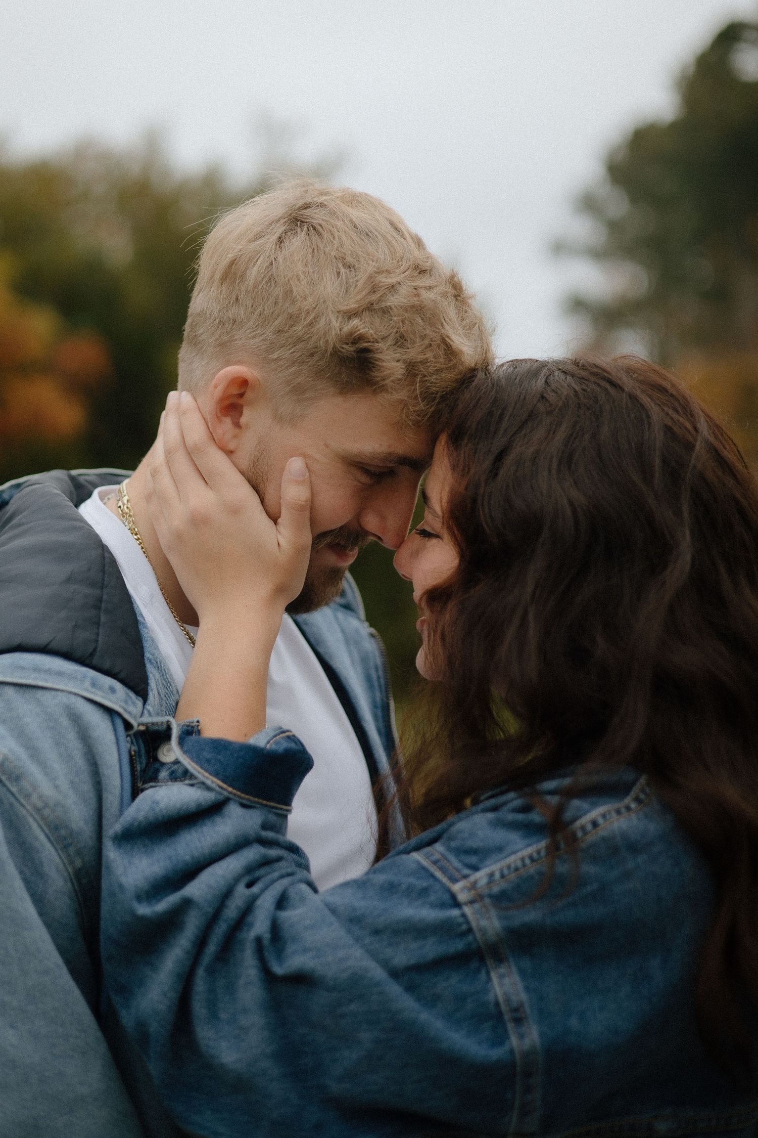 Intimate close-up moment between couple wearing denim jackets in an autumn setting.