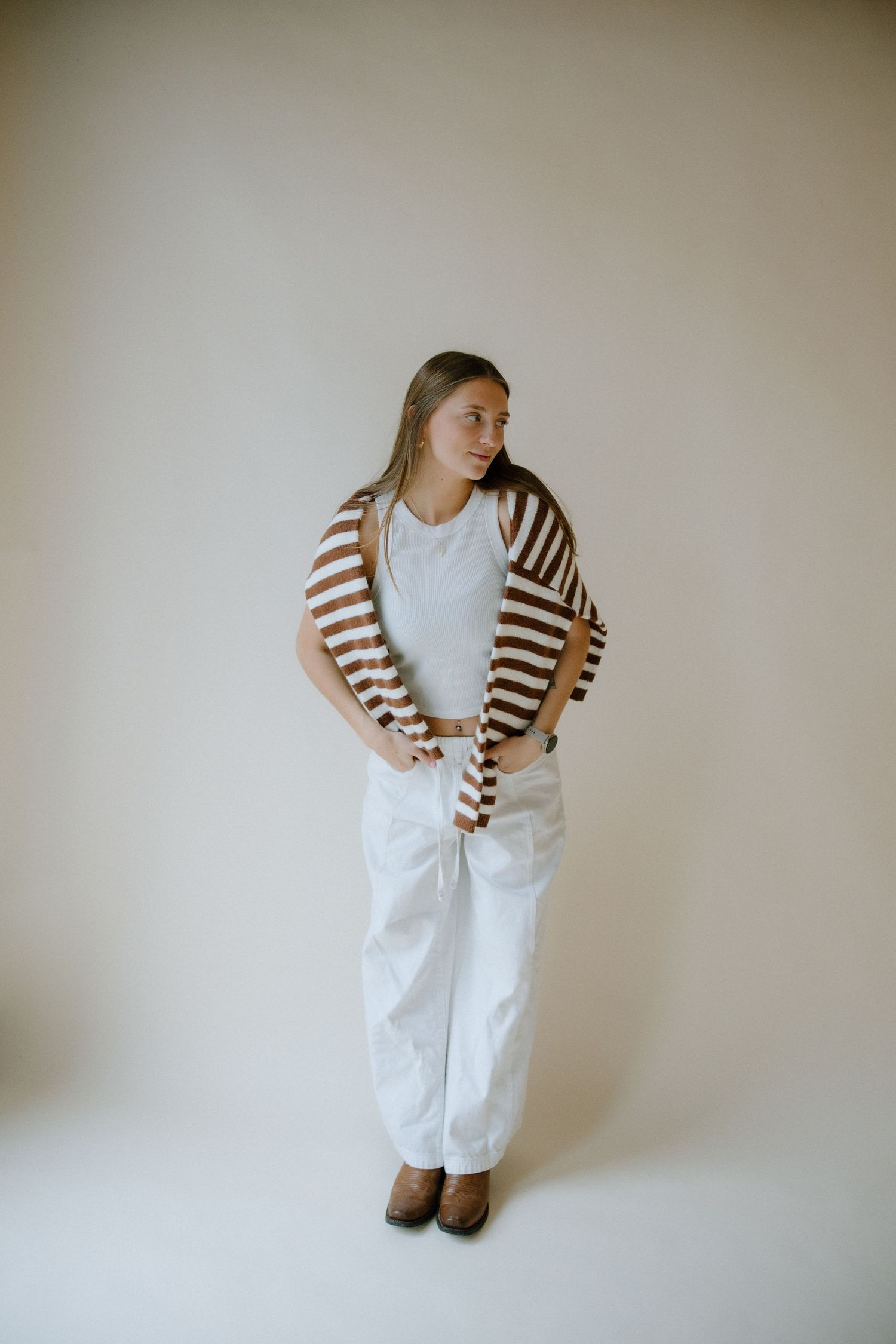 A person wearing a striped brown and white cardigan with white pants poses in different positions against a light wall.