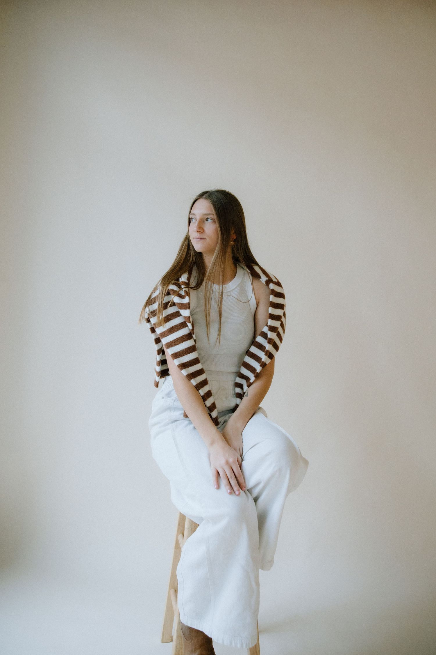 A fashion model poses against a neutral wall wearing a brown and white striped cardigan over white clothing.