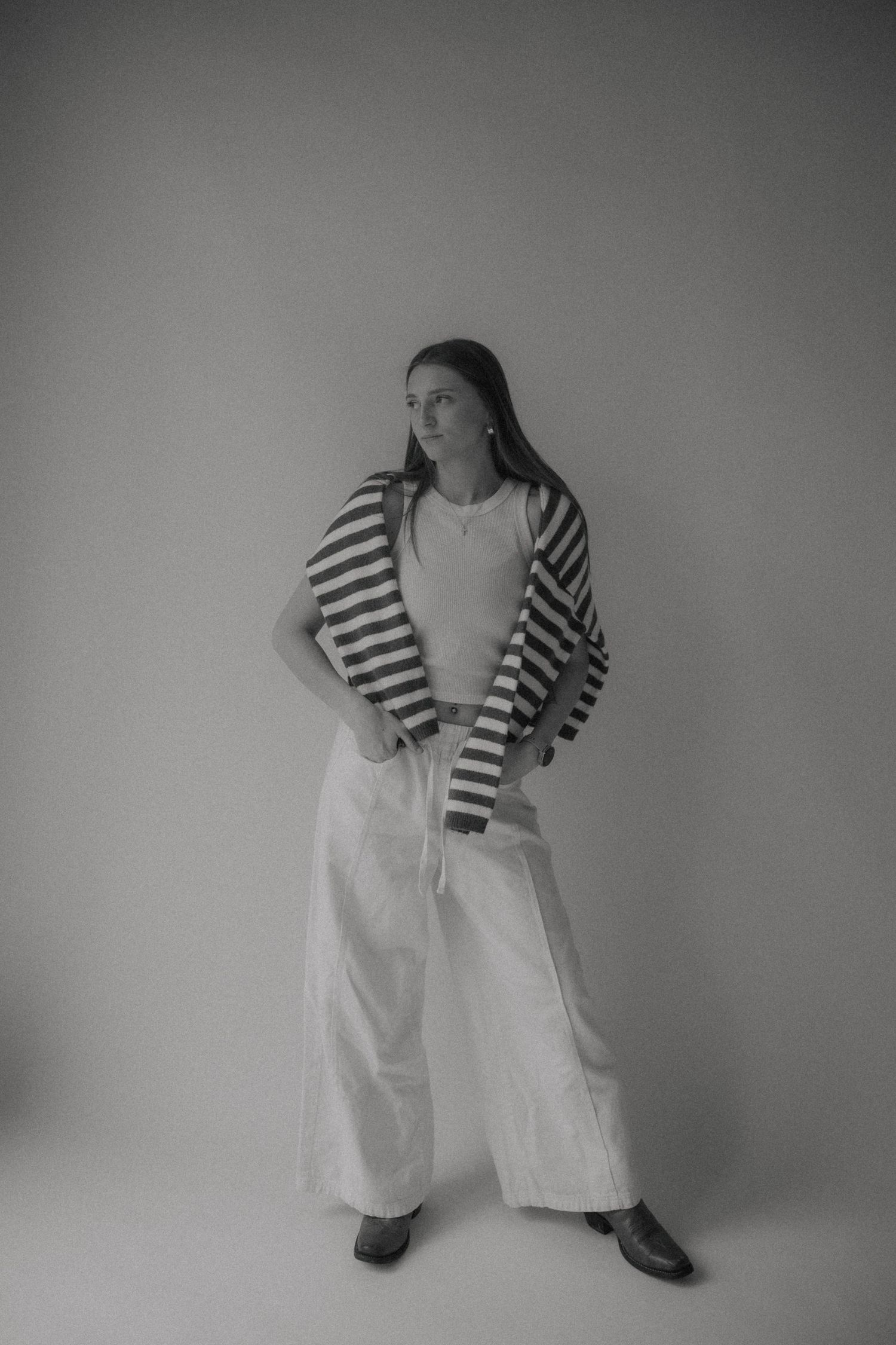 Black and white fashion photo showing a person in striped cardigan and wide-leg white pants against plain backdrop.