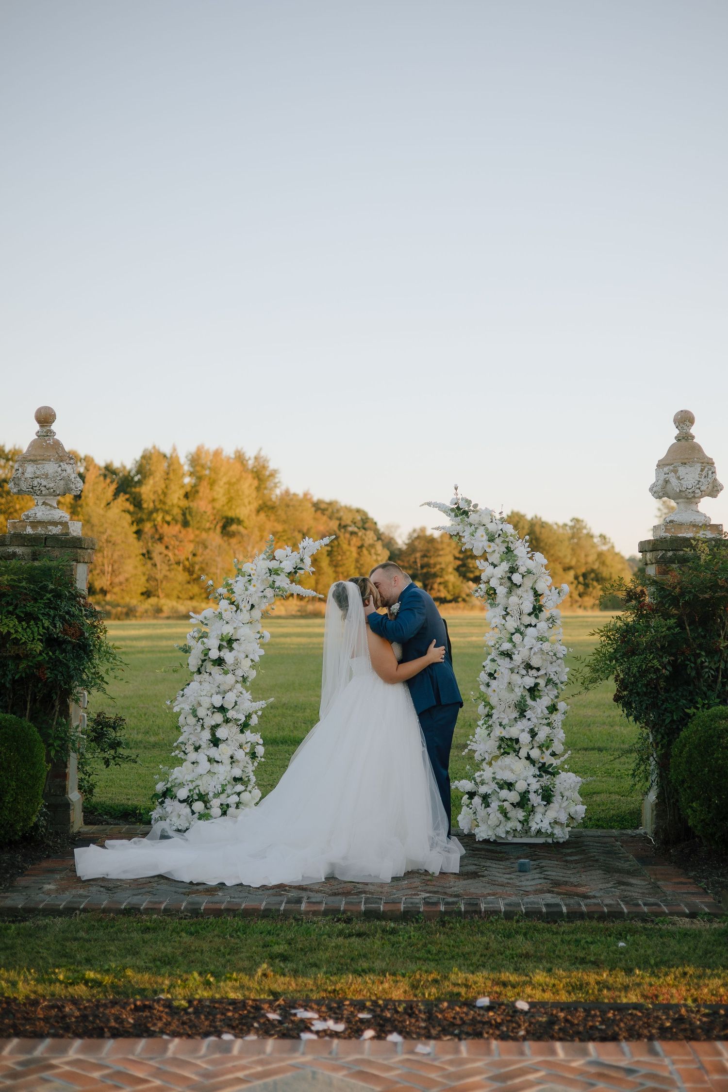 Wedding couple poses by floral arch during golden hour.