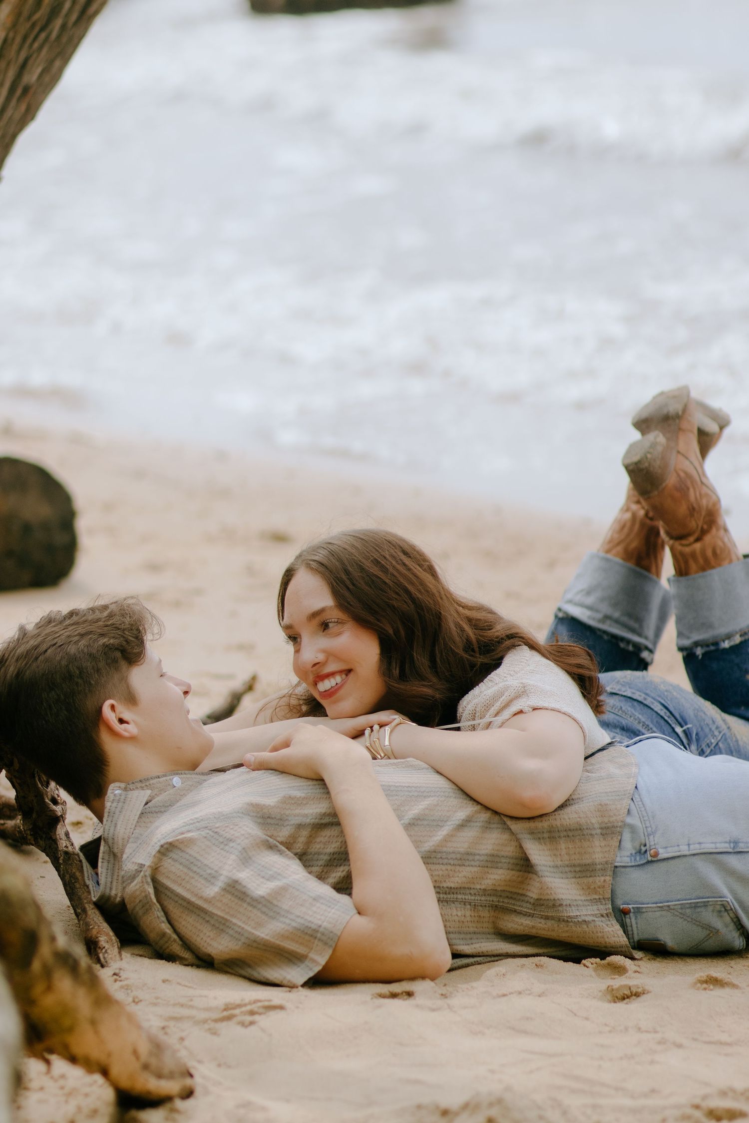 Two people lying on sand having a relaxed conversation together.