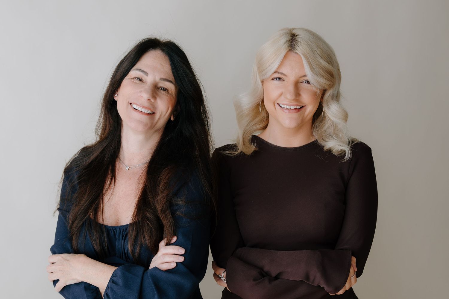 Two people wearing dark colored tops smile while posing together for a casual portrait.