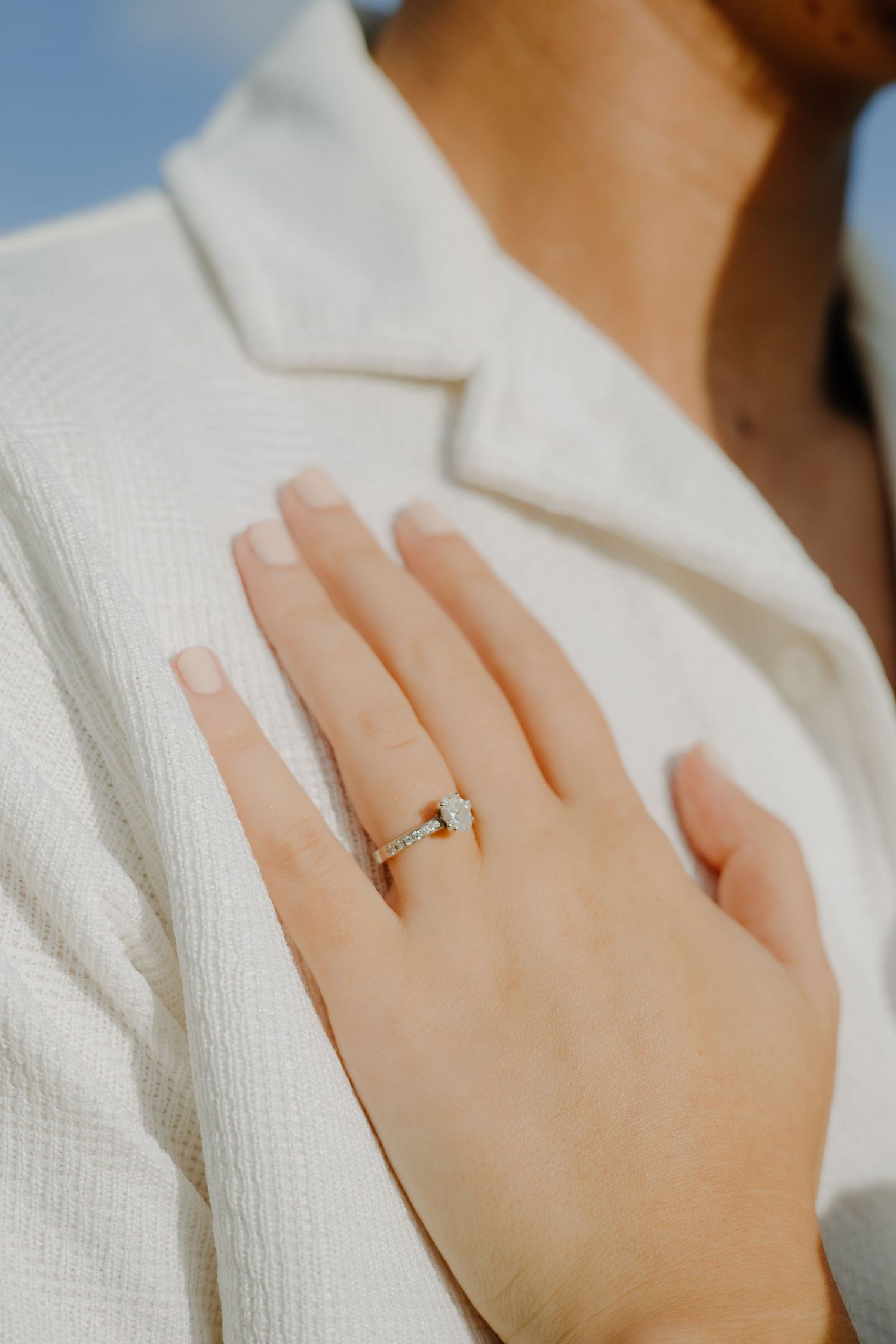 Close-up shot of a delicate engagement ring on a hand against white fabric.