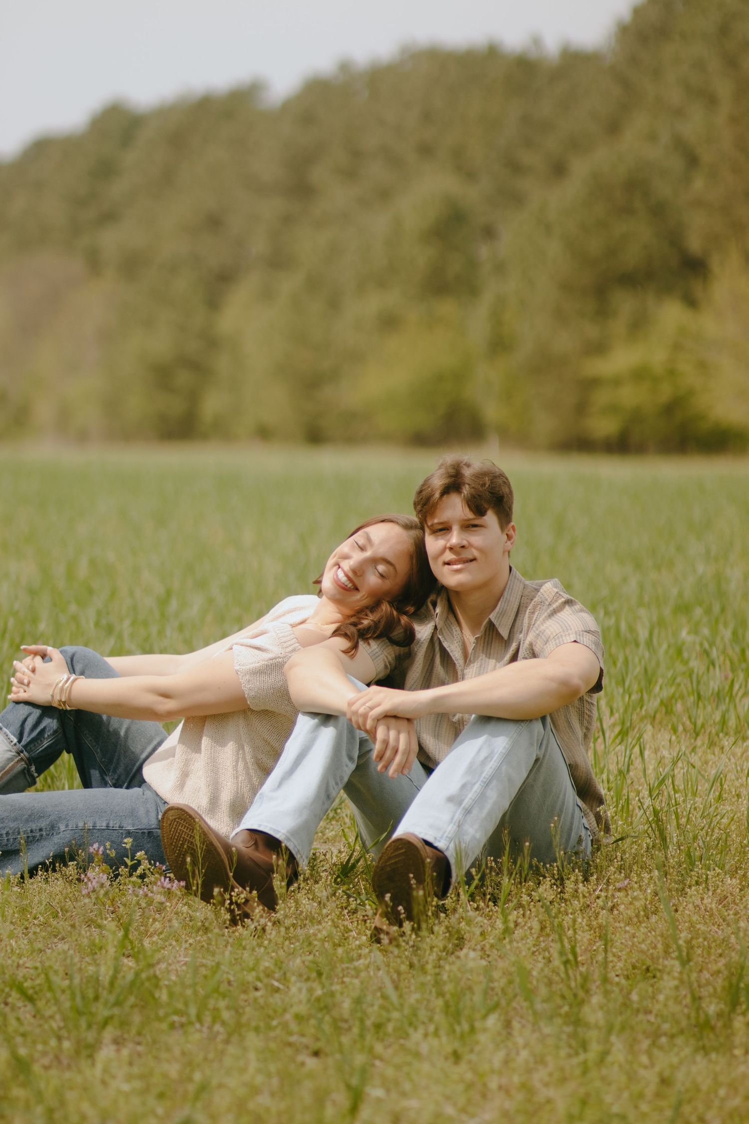 A couple sitting close together in a sunny meadow with wildflowers.