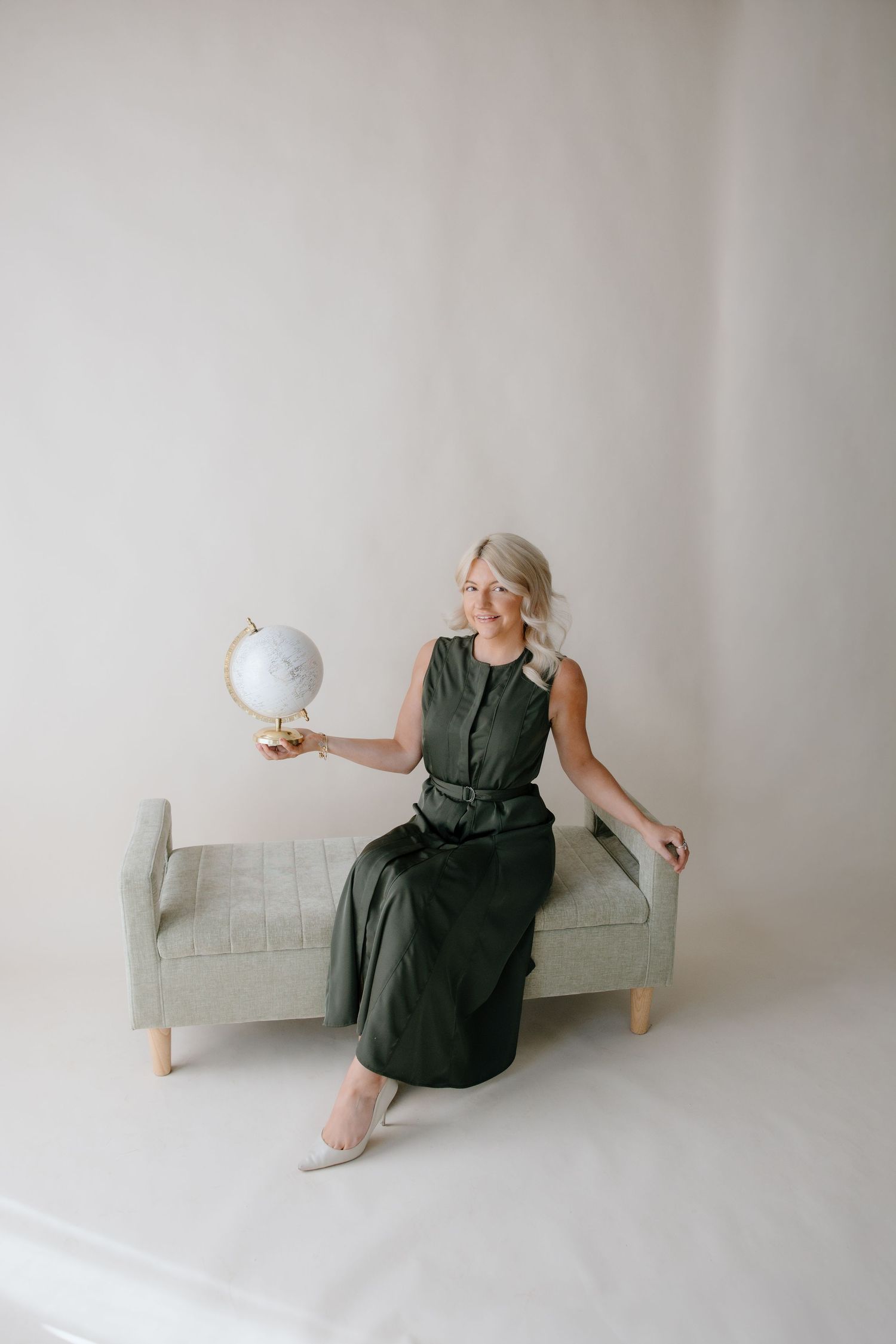 A series of four minimalist photos showing a person in a dark green dress sitting on a light gray sofa in a white room.