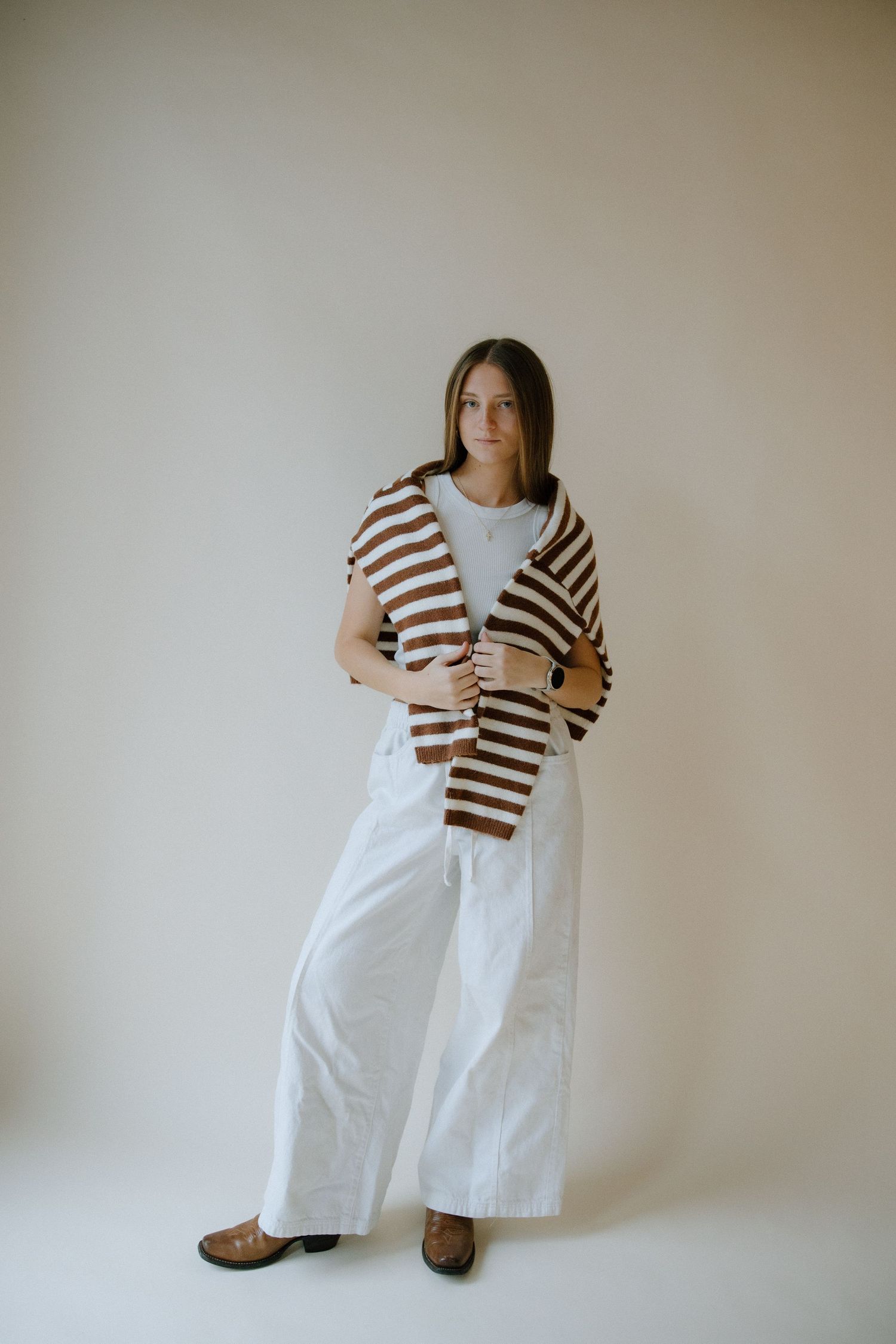 Striped brown and white cropped cardigan styled with high-waisted white wide-leg pants against neutral background.