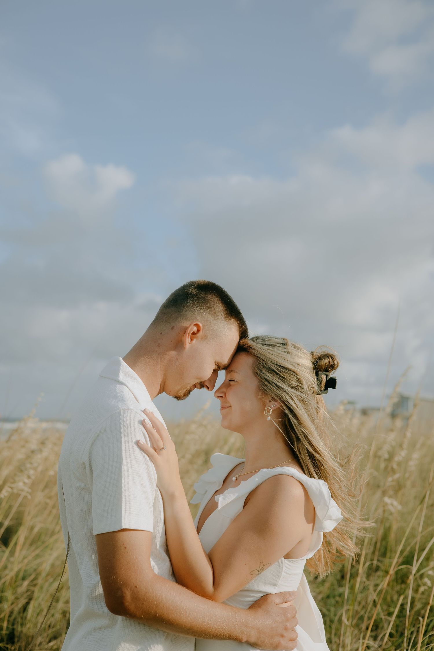 A romantic couple embraces in a wheat field under cloudy skies.