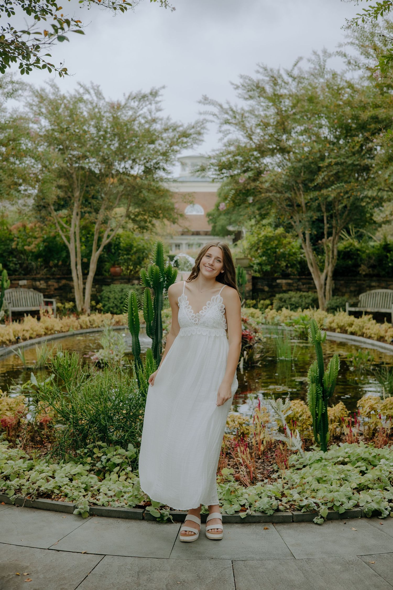 Person wearing white dress posing in landscaped garden with cacti and greenery.