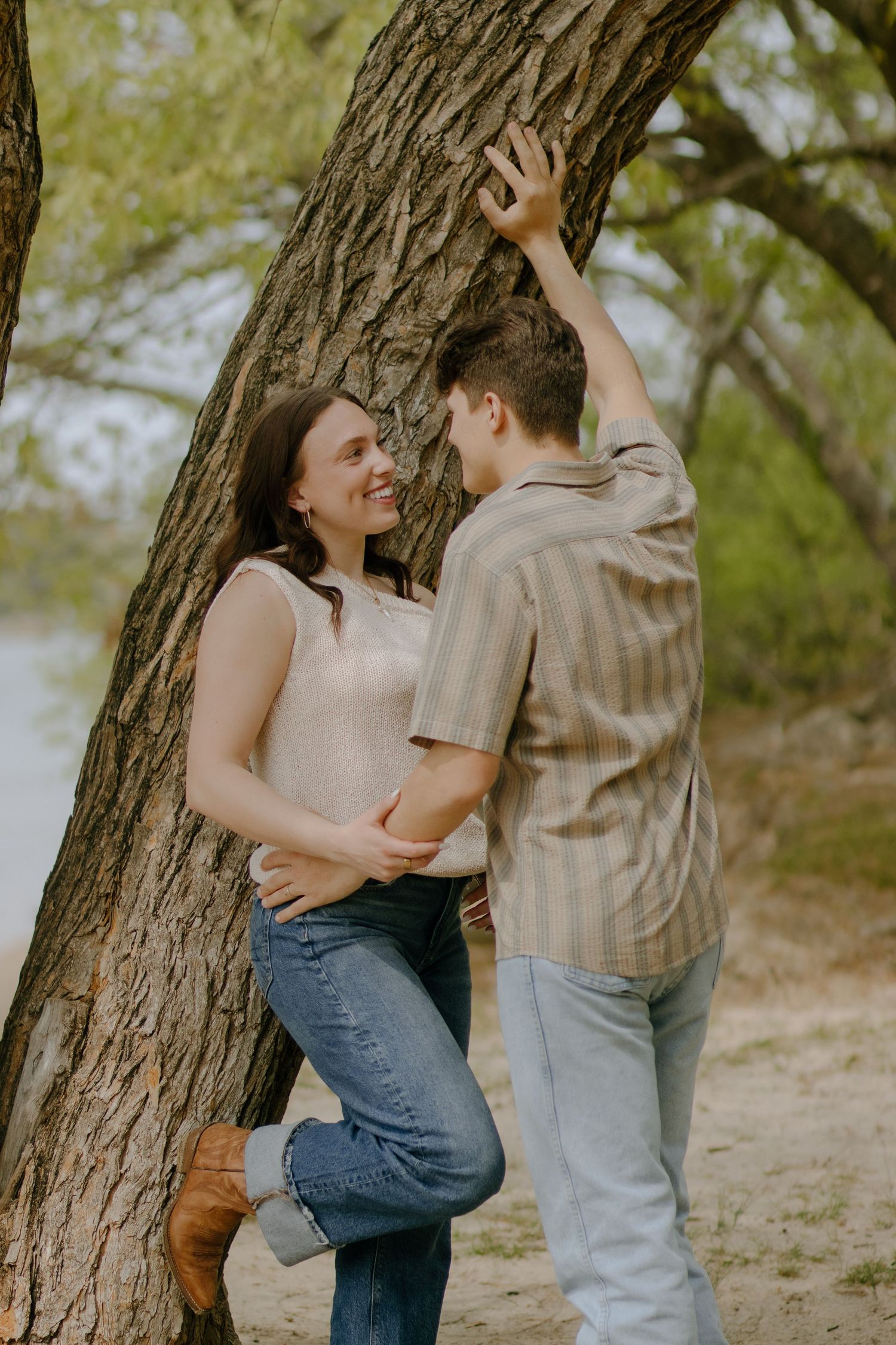 Two people playfully interact beneath a tree in a natural outdoor setting.