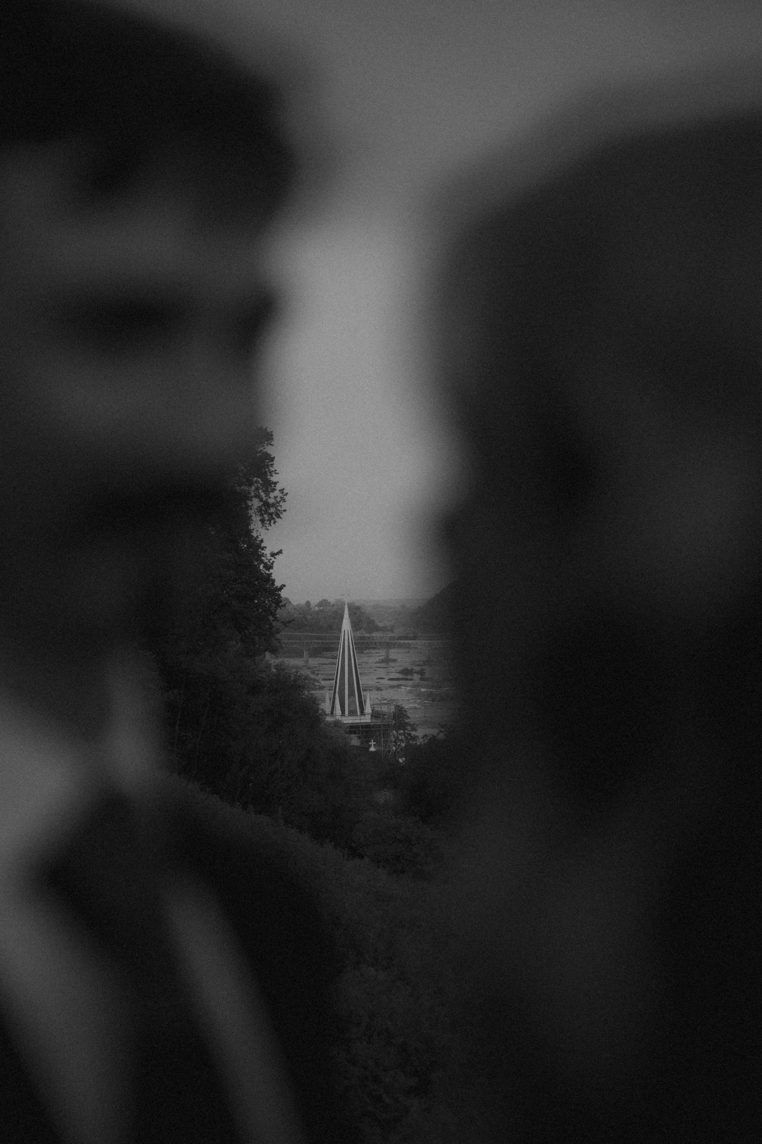 Black and white photo of two blurred men framing a distant church steeple surrounded by trees.