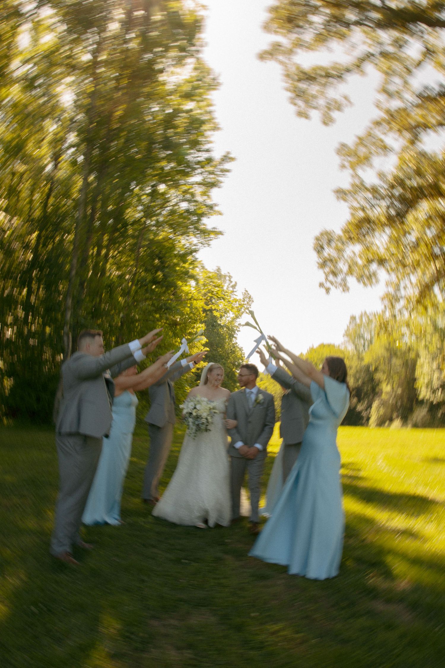 Wedding party celebrating outdoors in summer, raising hands over bride and groom at Avonlea Farms in Mineral, VA. Cinematic wedding photos