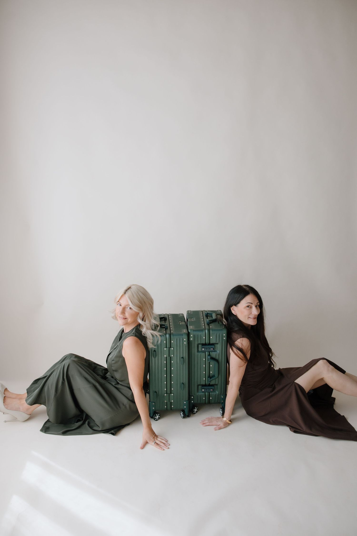 Two models in casual dresses pose on a white backdrop with green storage crates between them in an artistic series.
