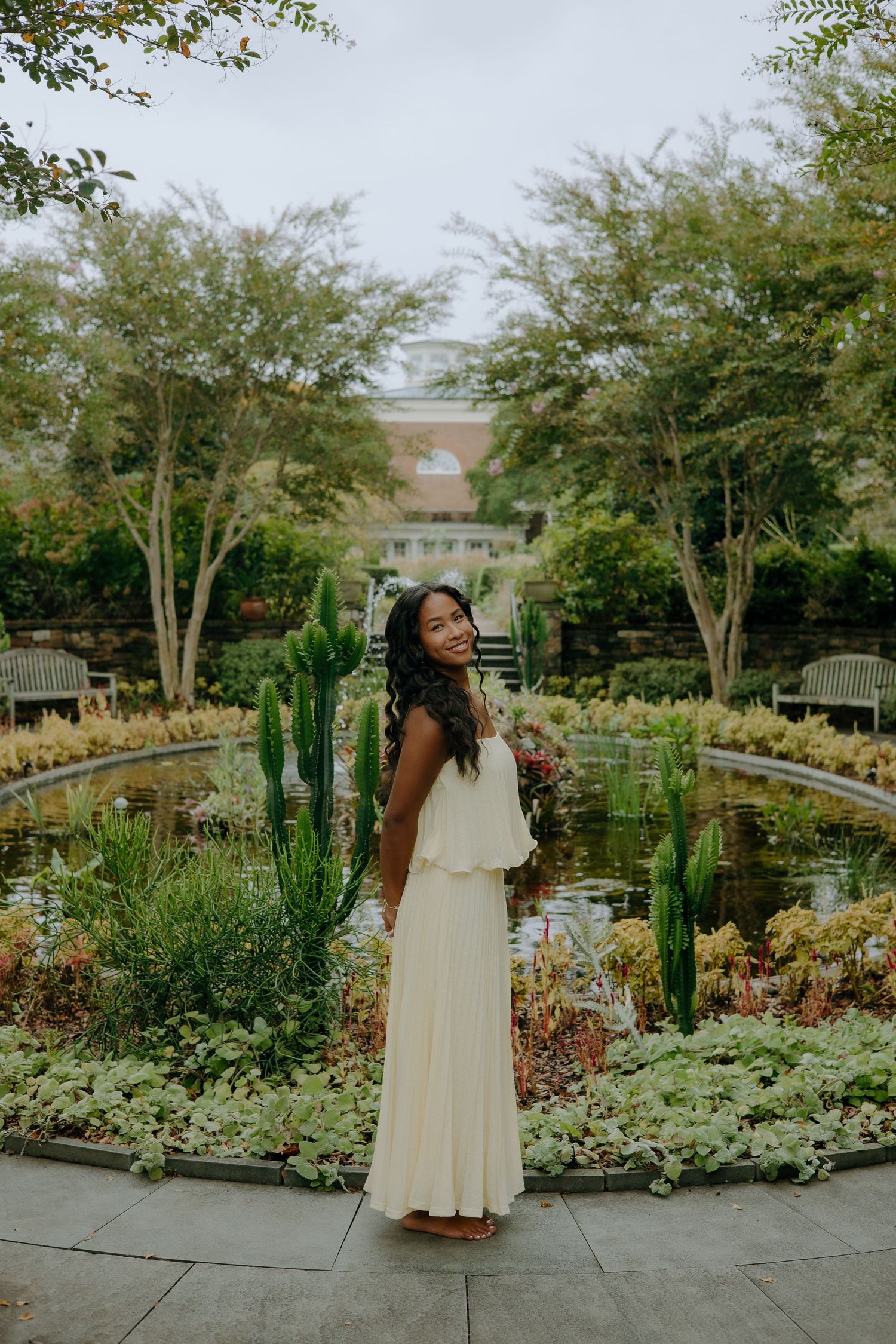 Person in cream dress standing in garden with cacti and varied plants.