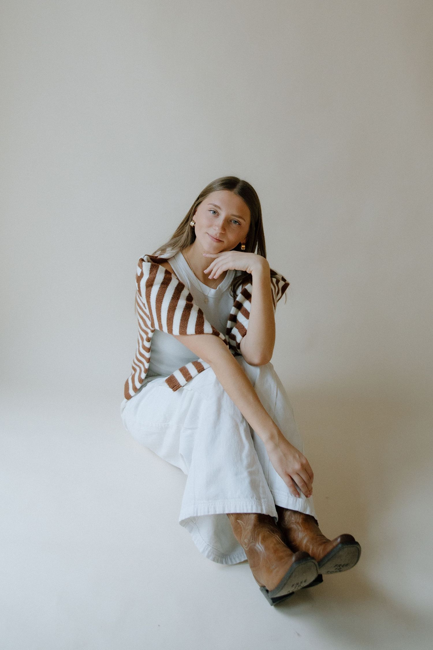 A person in a white dress and striped top sits against a plain wall in a series of minimalist poses.