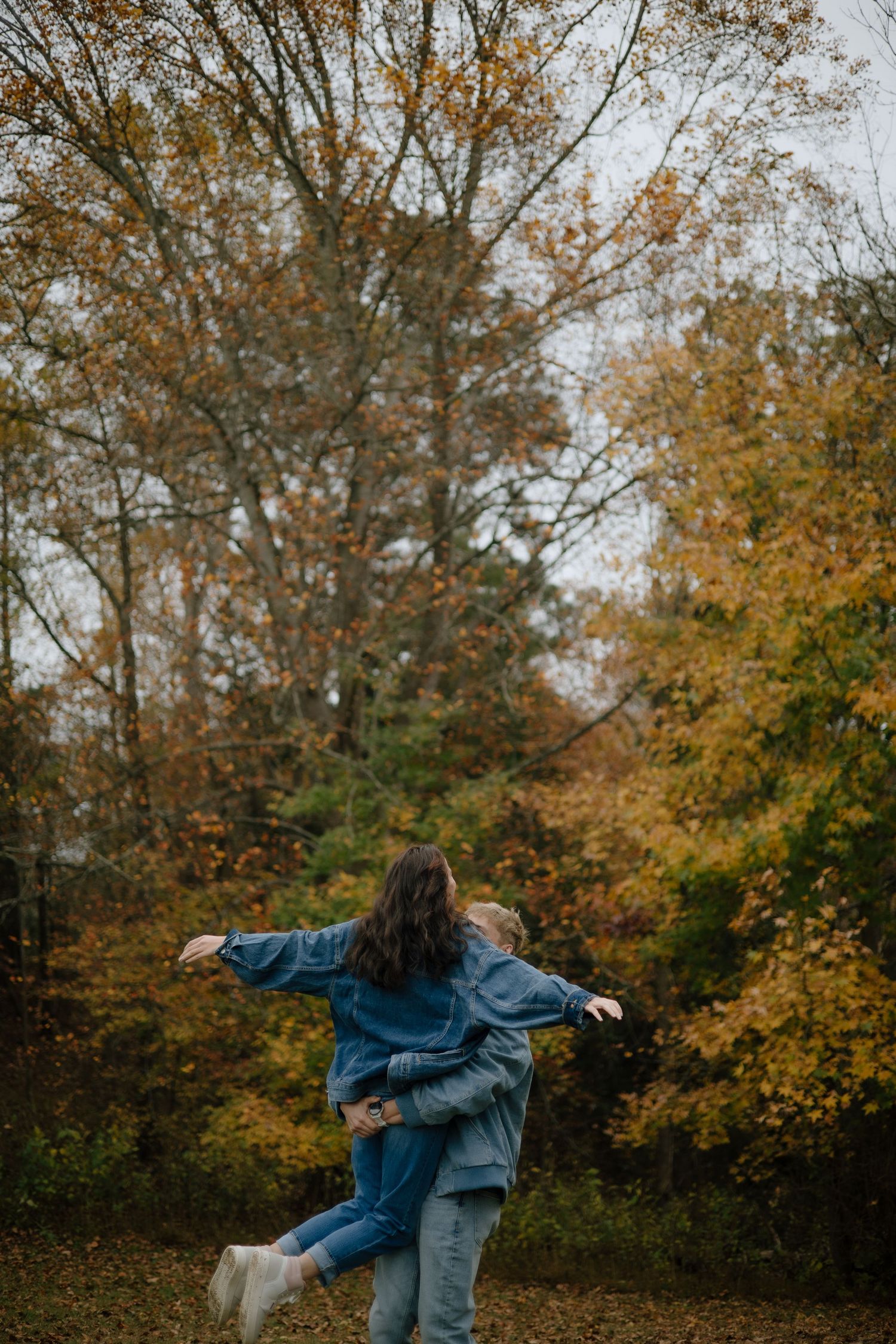 Person in denim jacket dancing expressively among autumn trees.