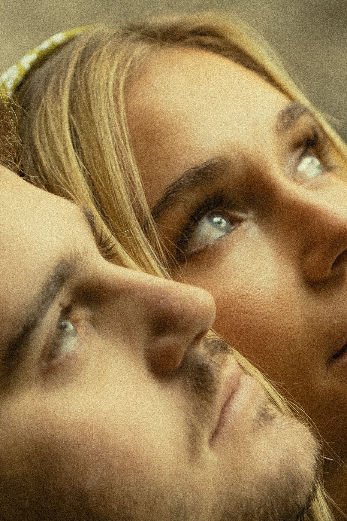 Close-up portrait of a young blonde woman and brunette man with blue eyes gazing upward together.