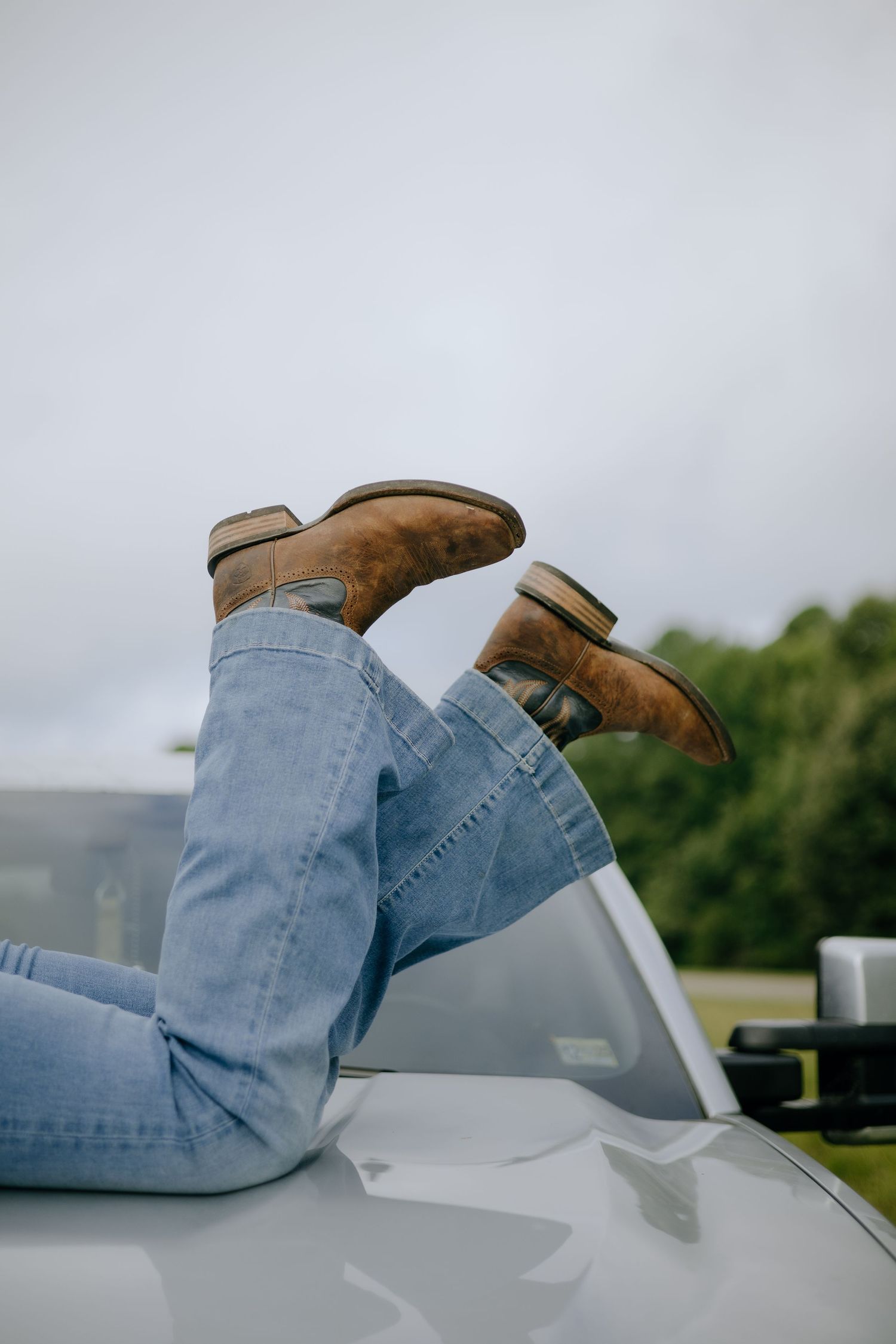 Blue jeans and brown boots resting on a white surface with sky in background.