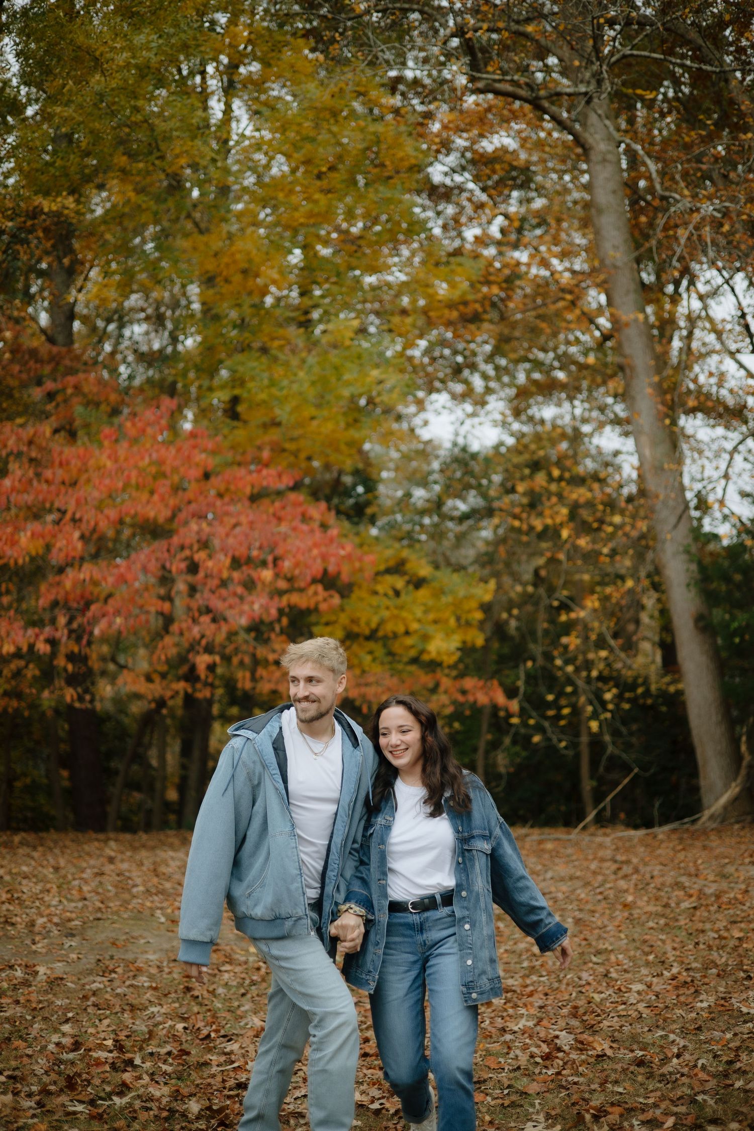 Couple holding hands and walking through a colorful autumn forest with red and yellow foliage.