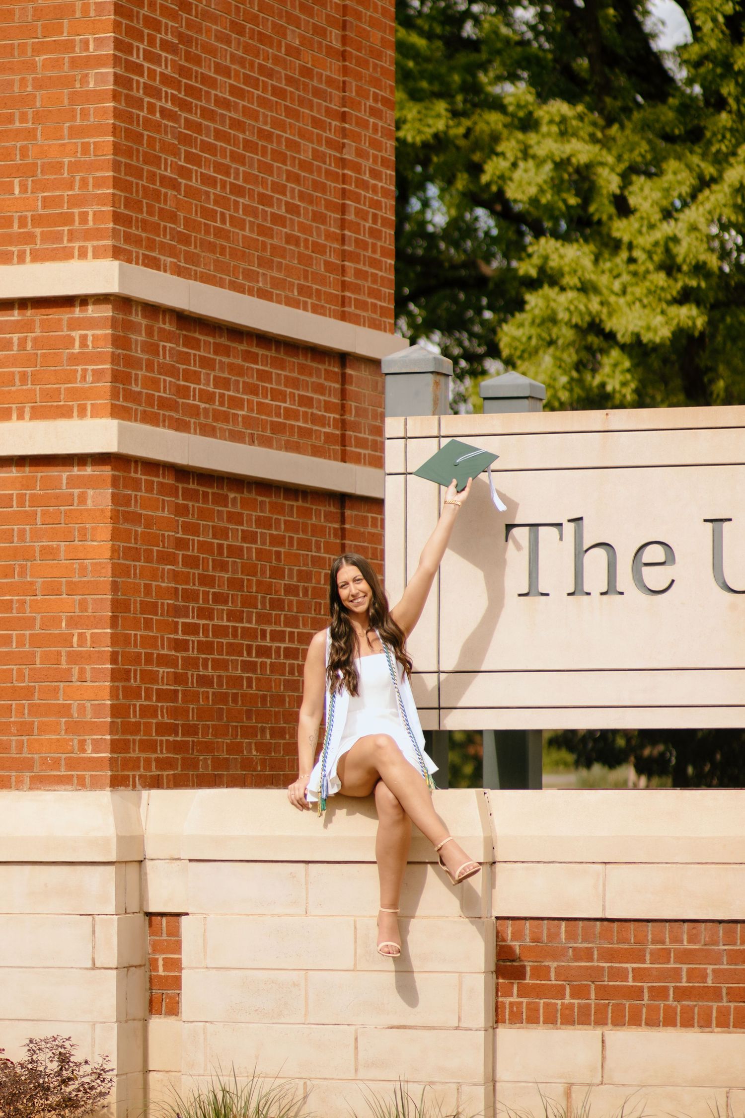 A person poses playfully near a brick and stone university entrance sign.