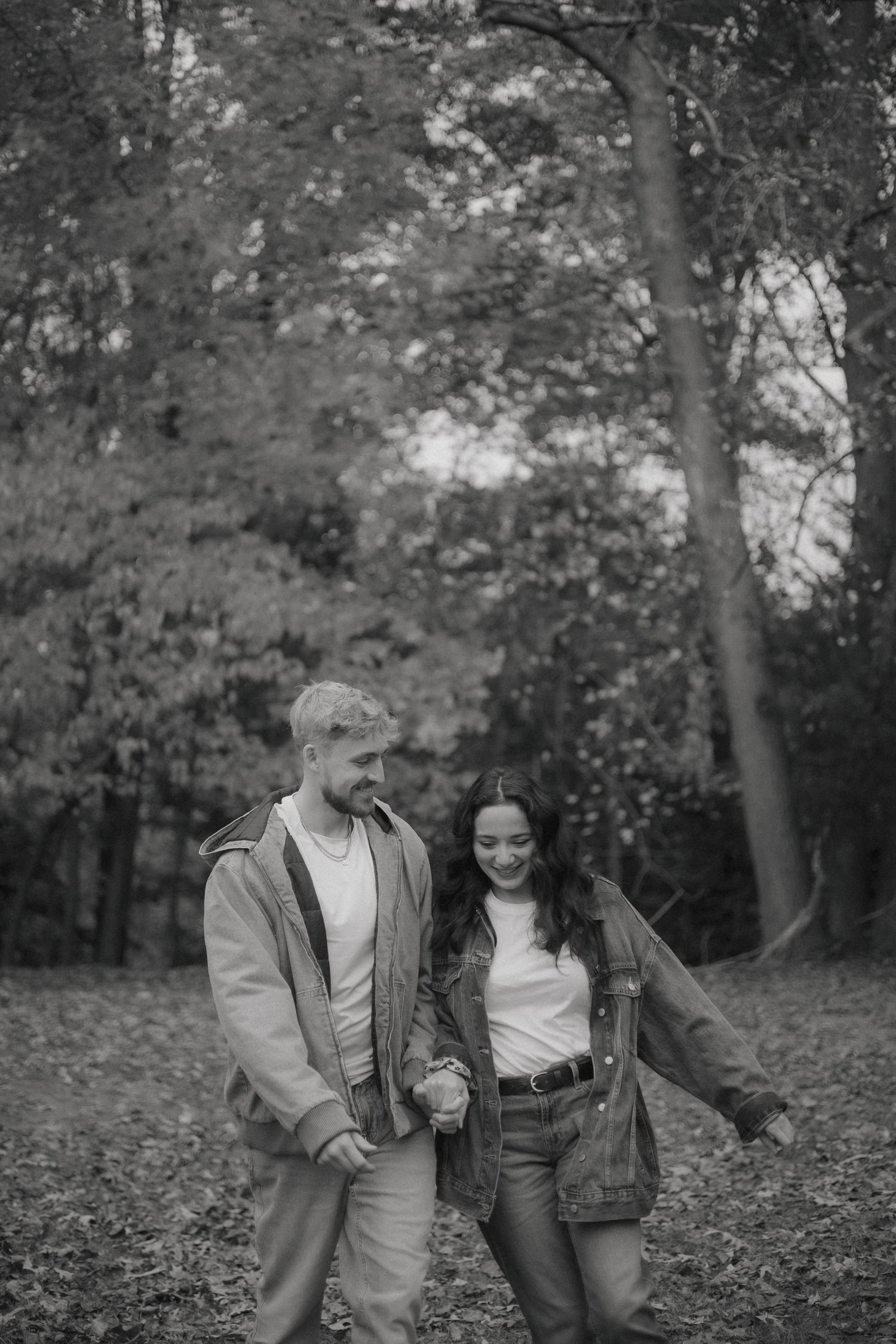 A couple walks together through a wooded area in autumn, sharing intimate moments across multiple black and white photos.