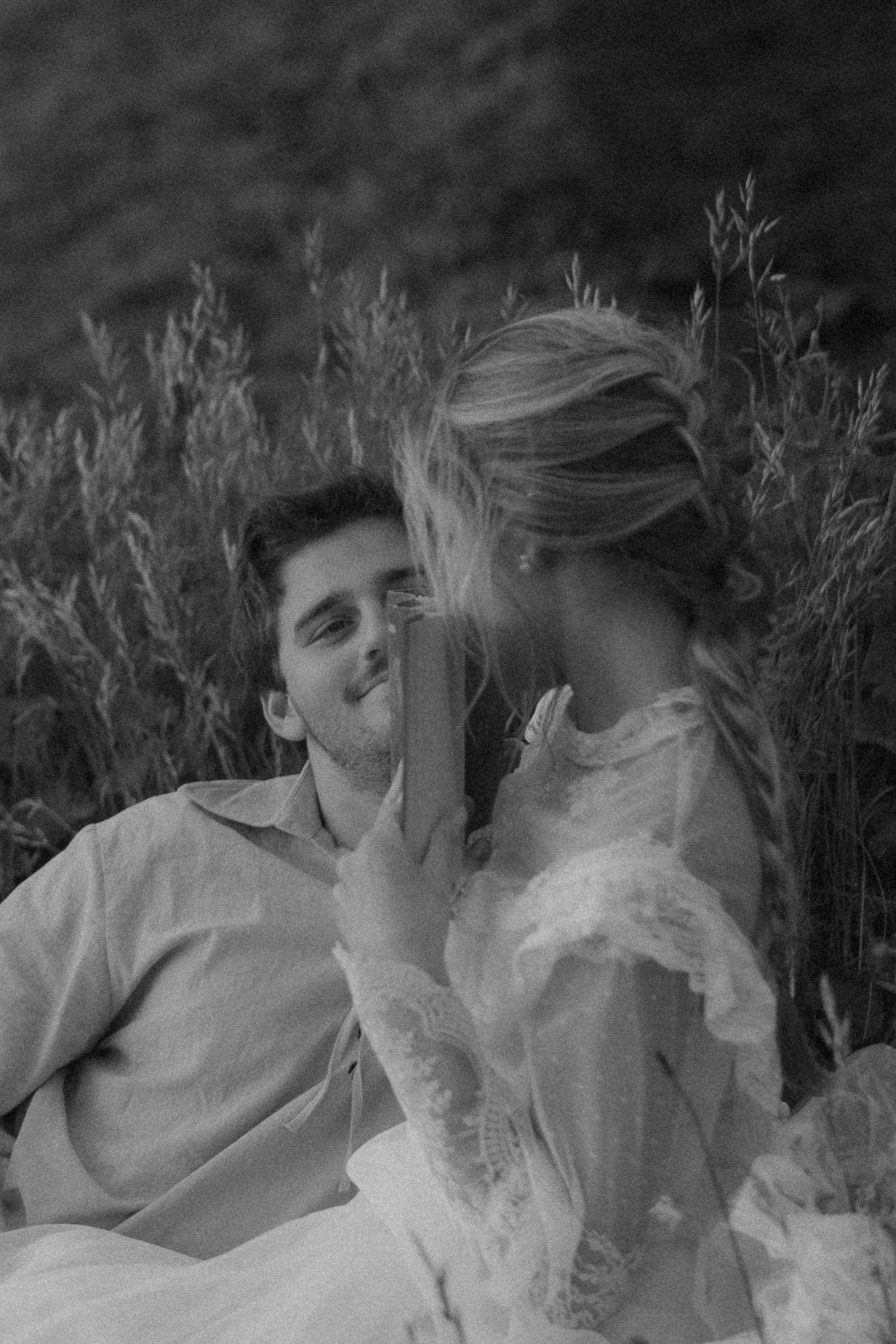 Black and white photo of a romantic couple sitting in a field, woman gently touching mans face.