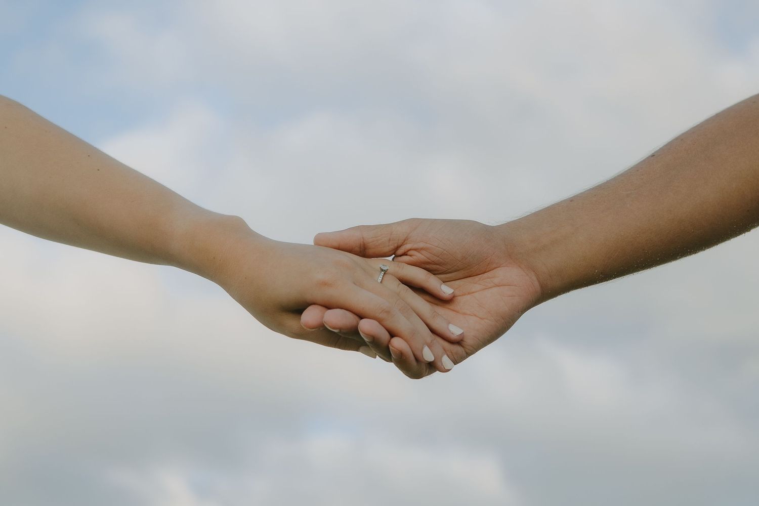 Two hands reaching out to hold each other against a cloudy sky background.
