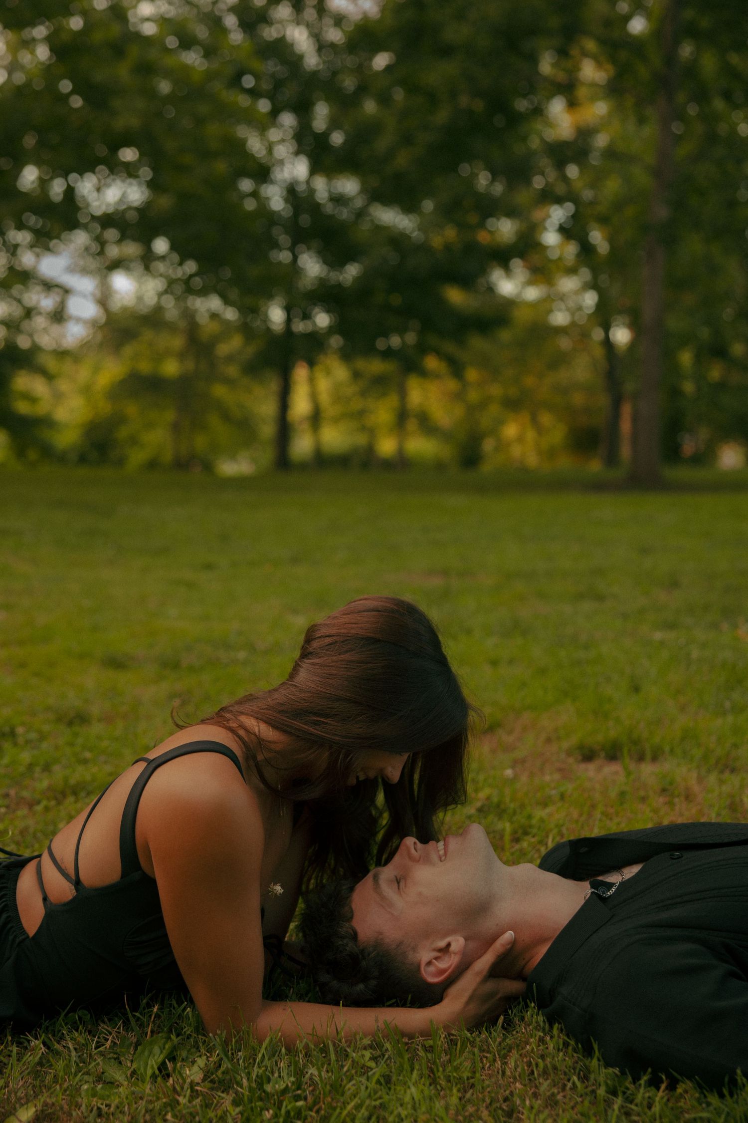 Romantic couple lying on grass in a park, woman leaning over man engagement session in fredricksburg, va. virginia engagement photographer
