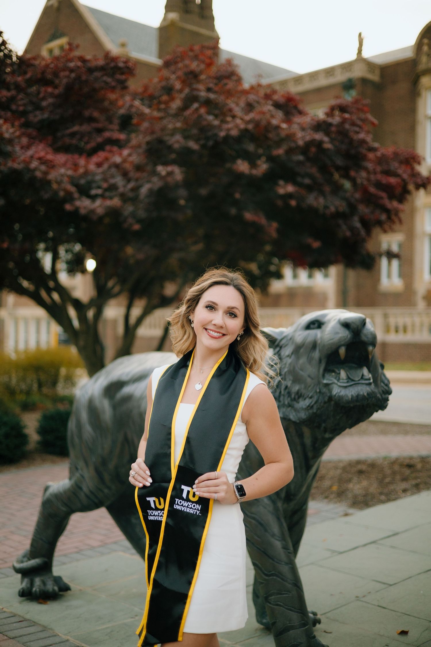 Graduate posing with bronze panther statue at university campus during graduation photo session.