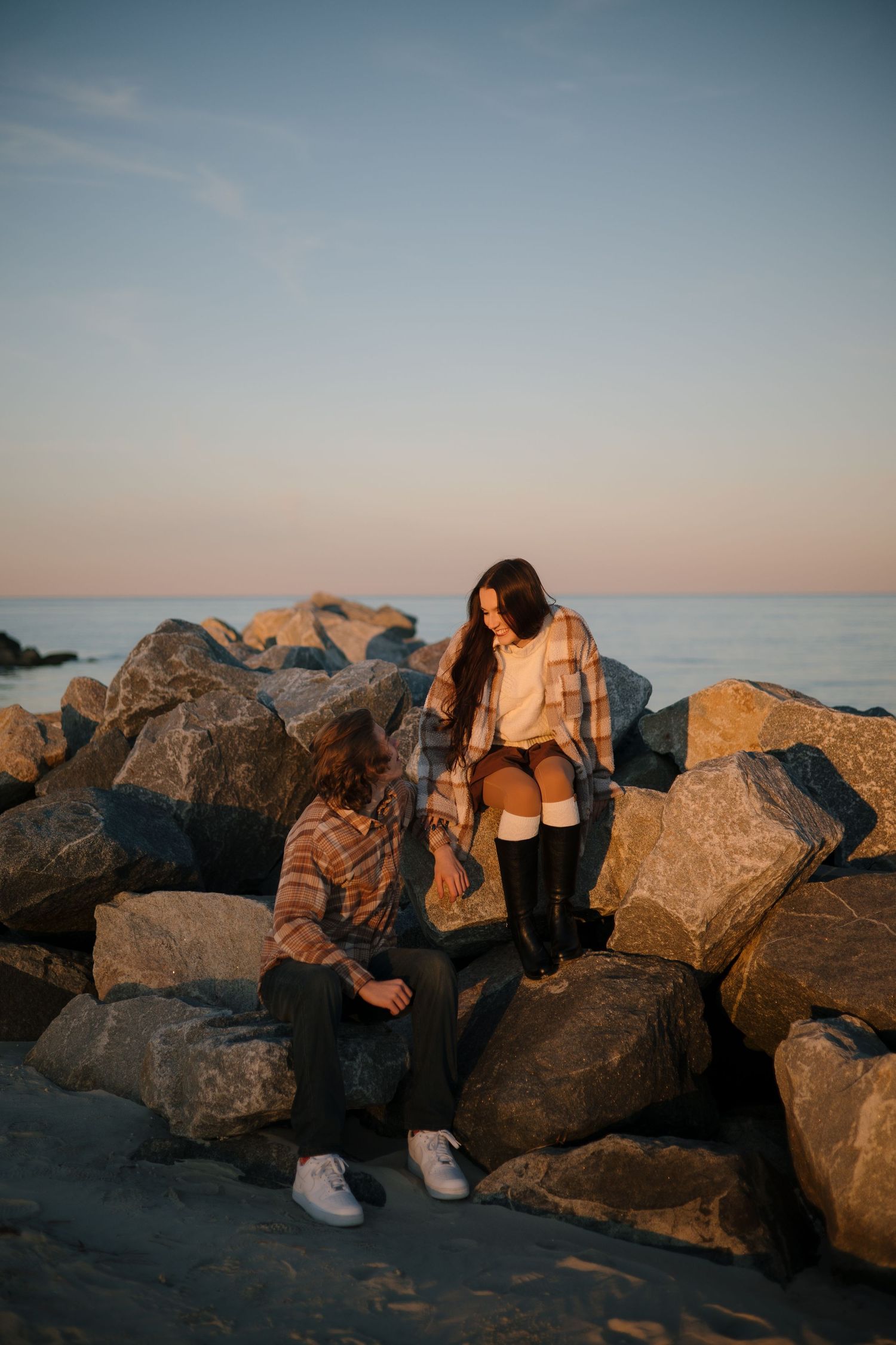 People sit together on large coastal rocks during sunset by the ocean.