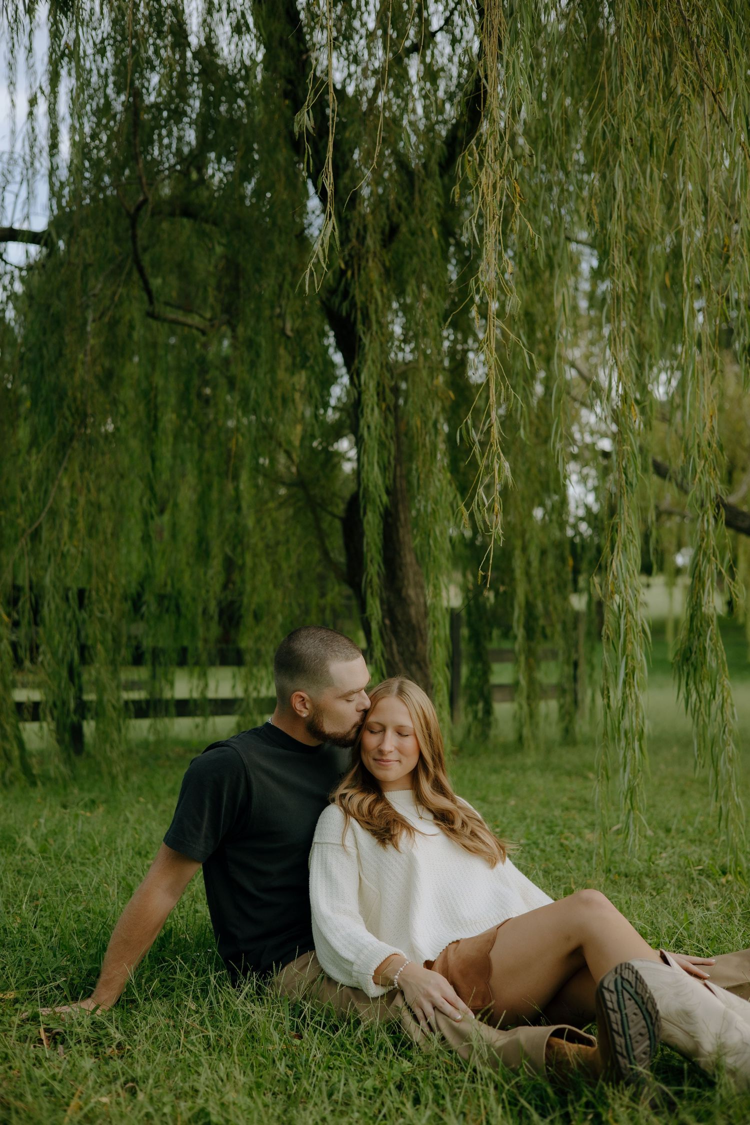 Romantic couple lounging together under a weeping willow tree in a park.
