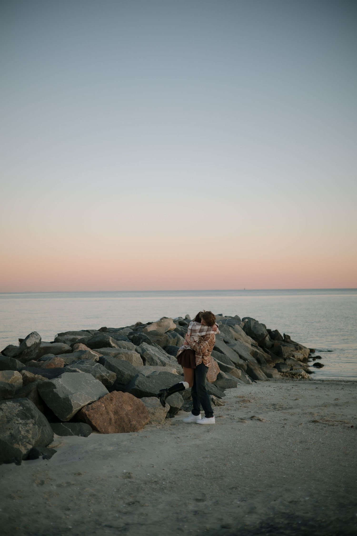 A distant view of people near rocky formations on a beach at sunset.