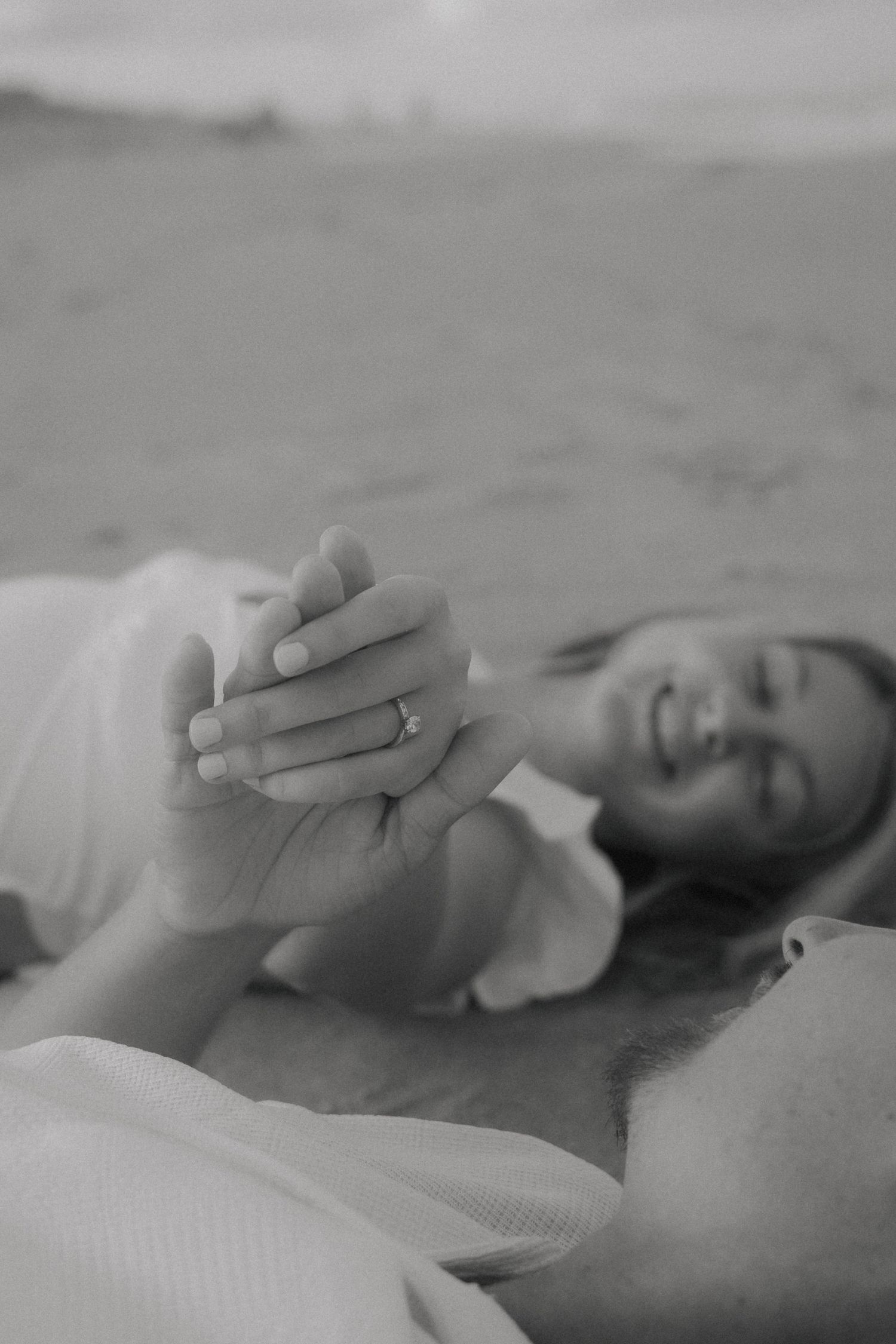 A black and white close-up shot of hands clasped together on the beach.