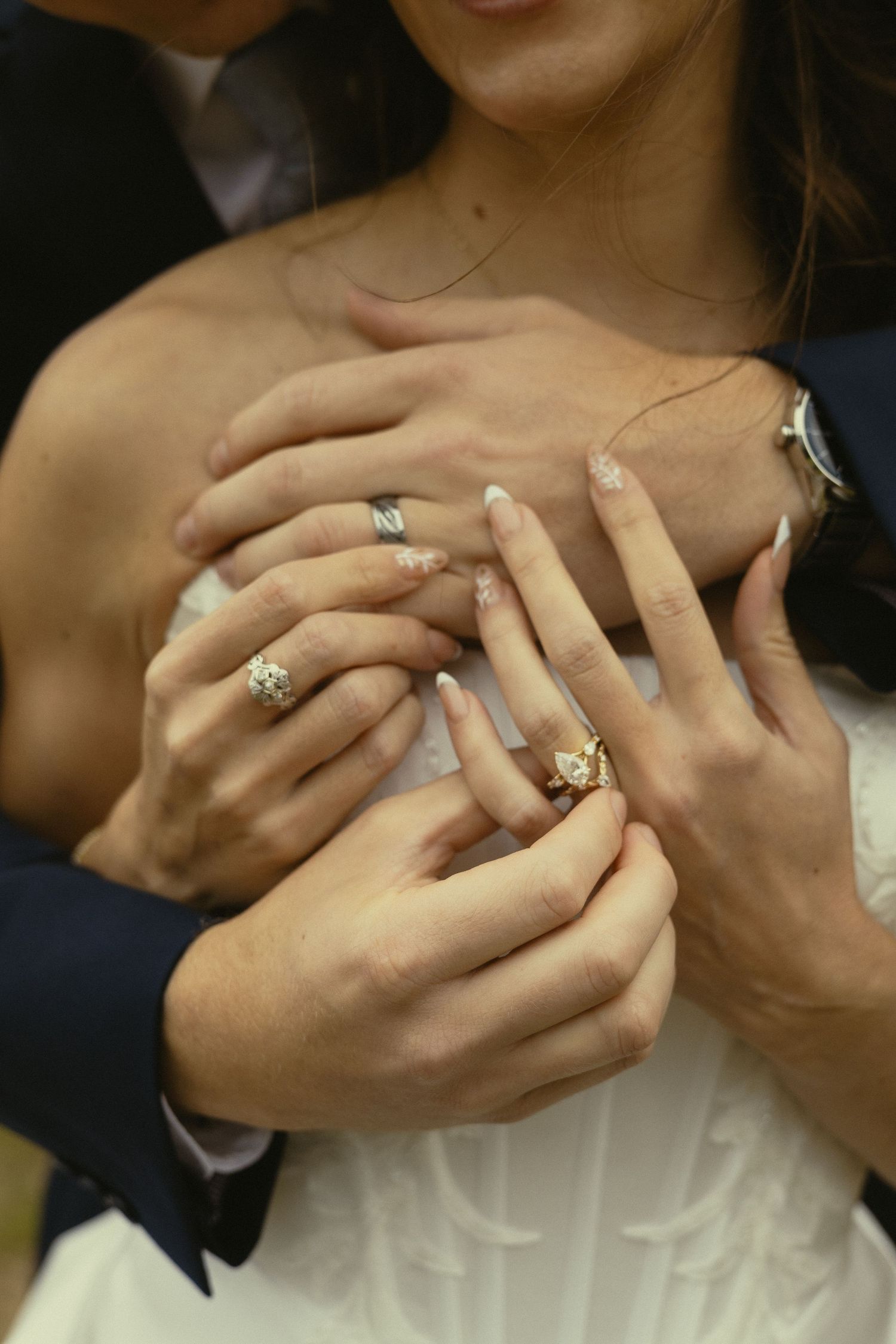 Bride and groom displaying wedding rings on intertwined hands, showcasing elegant diamond engagement ring and matching bands.