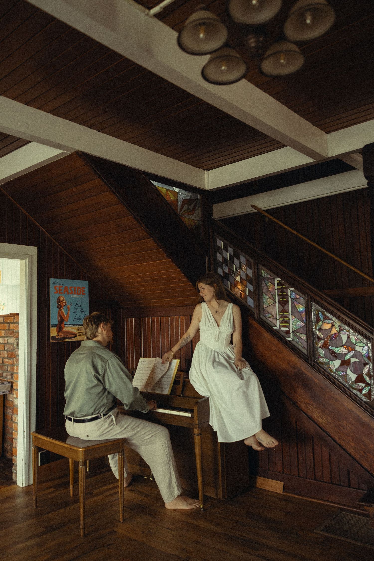 Couple sharing a romantic moment at a piano in a cozy wood-paneled room with stained glass staircase.