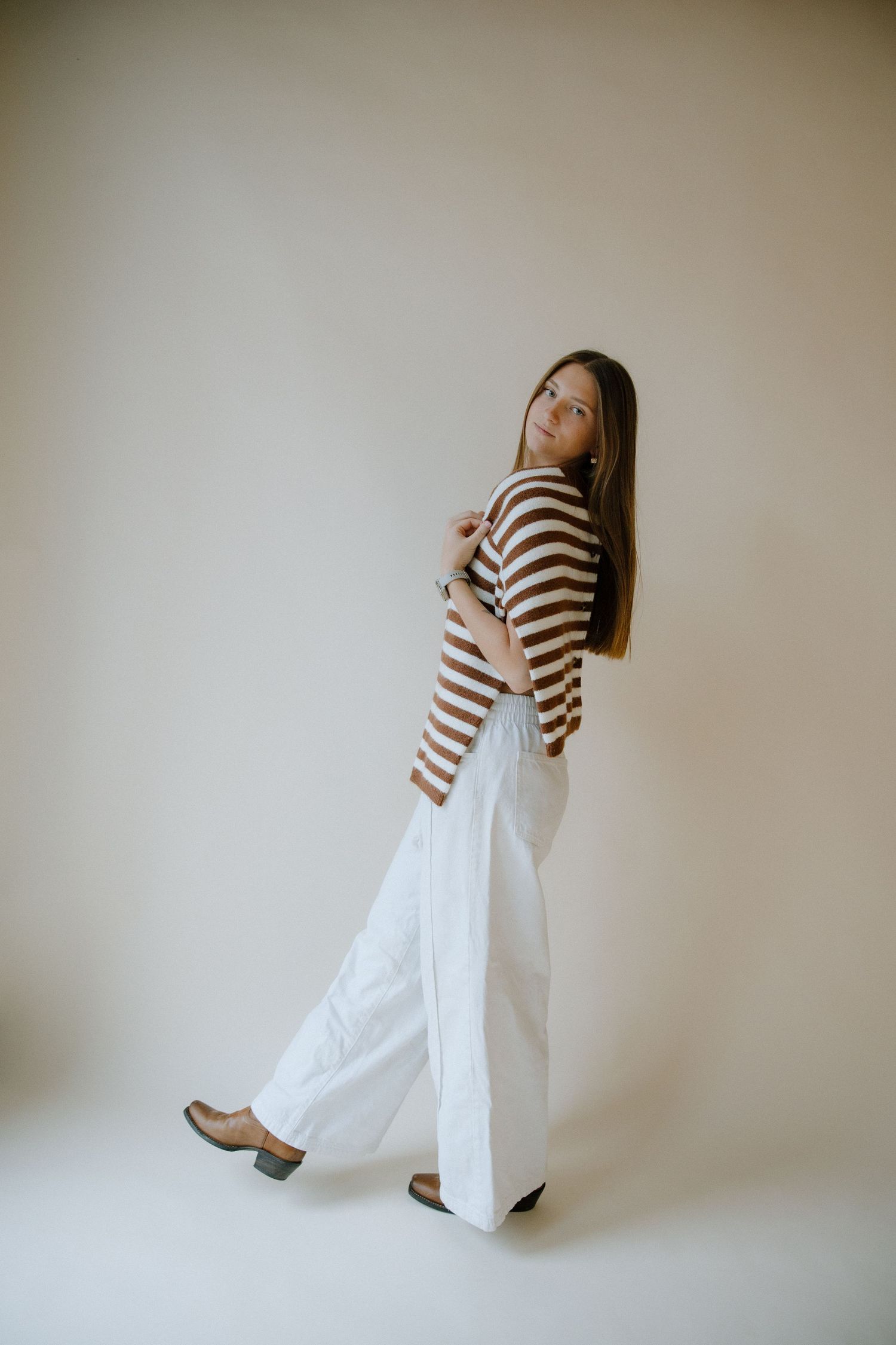 Person wearing striped top and white palazzo pants poses in different angles against neutral wall background.