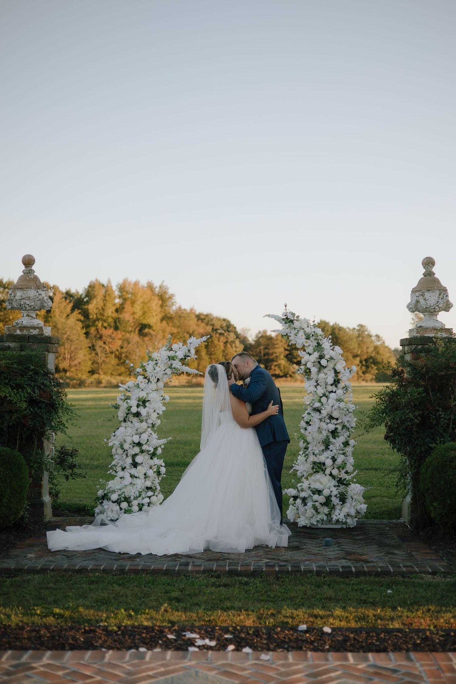 A wedding ceremony setup with white floral arches against an autumn landscape.