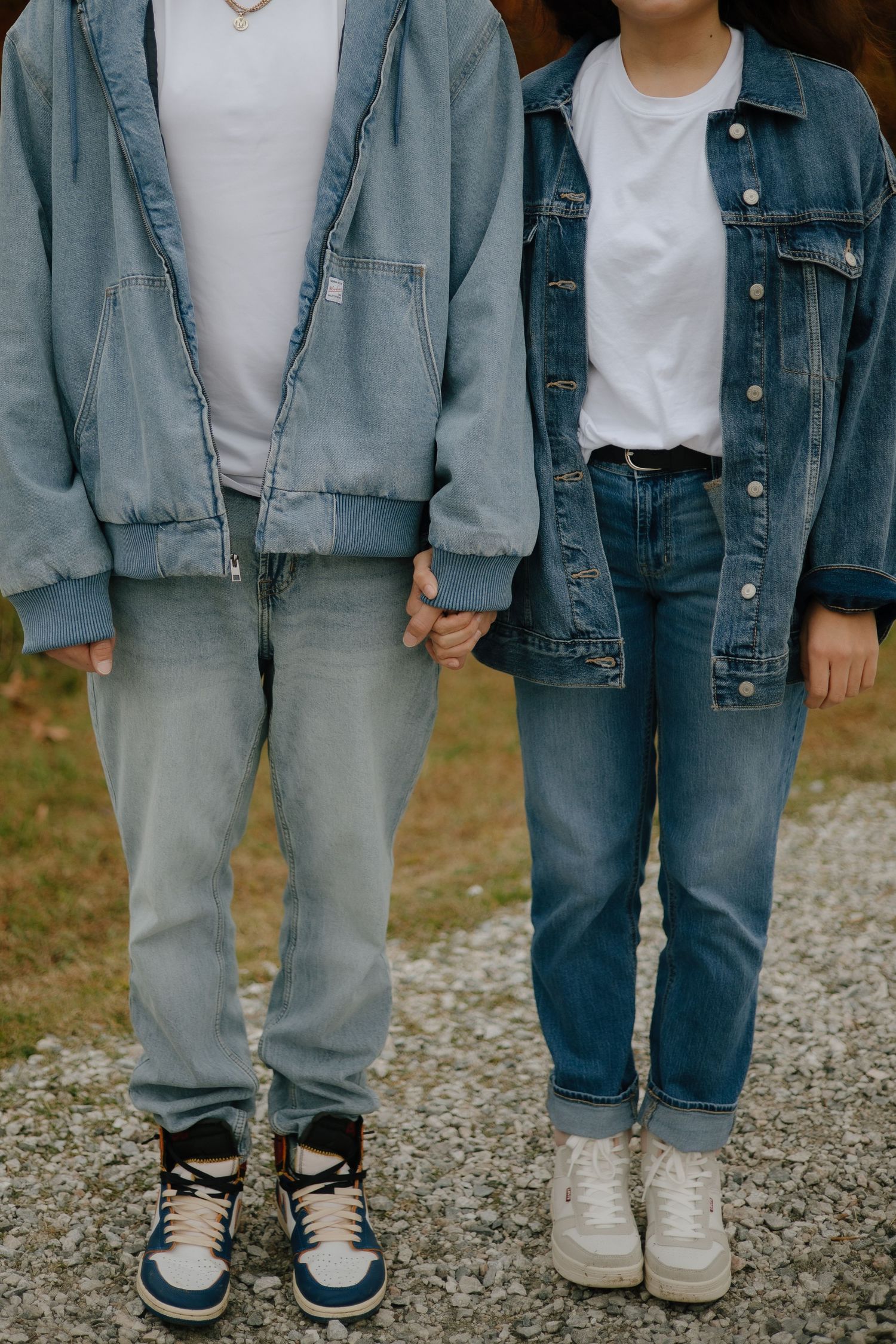 Close-up of two people wearing matching denim outfits and sneakers standing together.