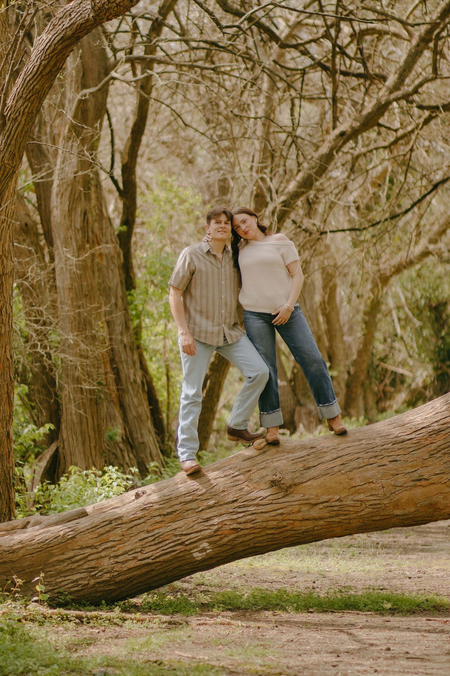 A couple sitting together on a fallen tree trunk in a wooded area.