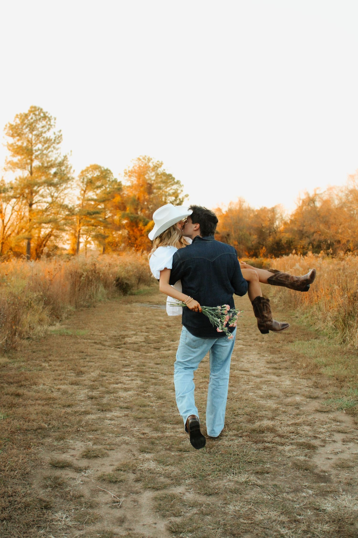 A couple shares a romantic moment on a dirt path during golden hour in an autumn field.