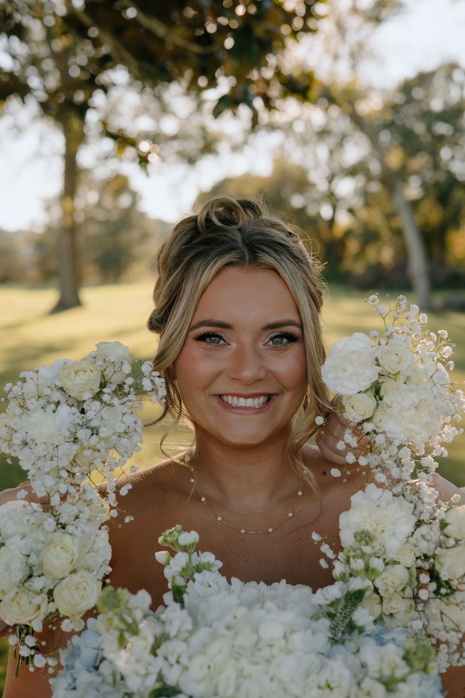 A creative wedding portrait featuring white flowers in the foreground framing a joyful outdoor bridal photo.