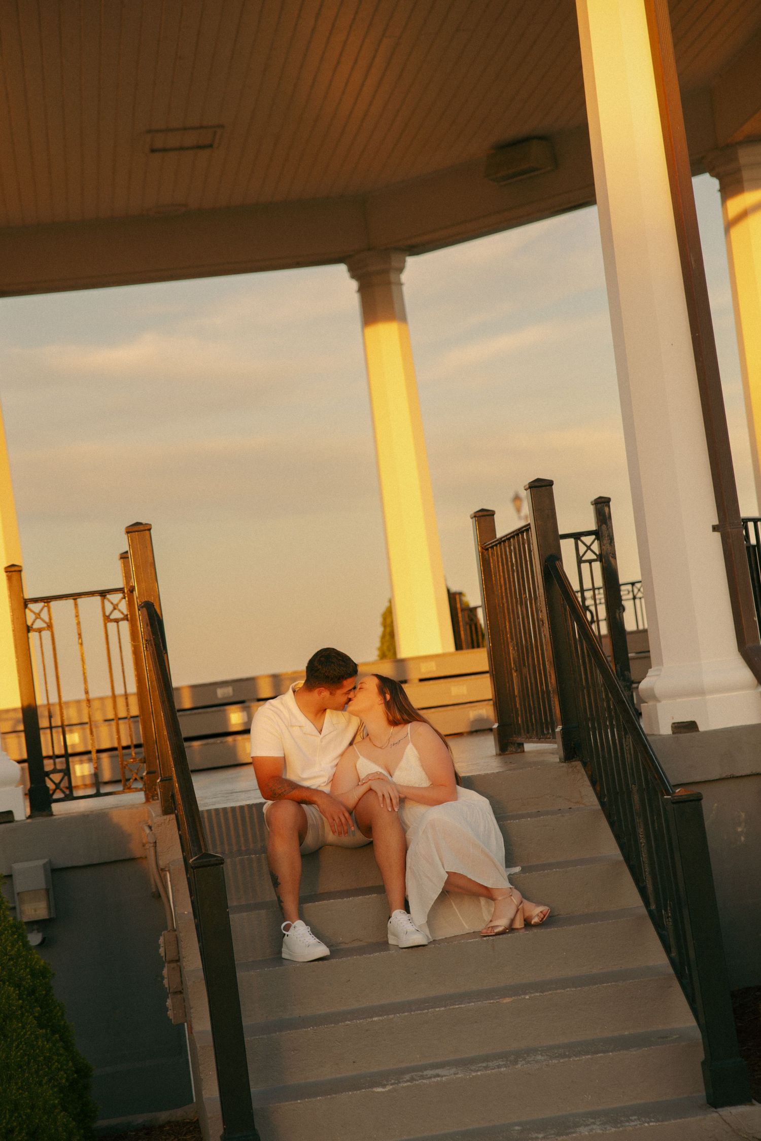 Couple sitting on gazebo steps sharing a romantic moment at golden hour sunset.
