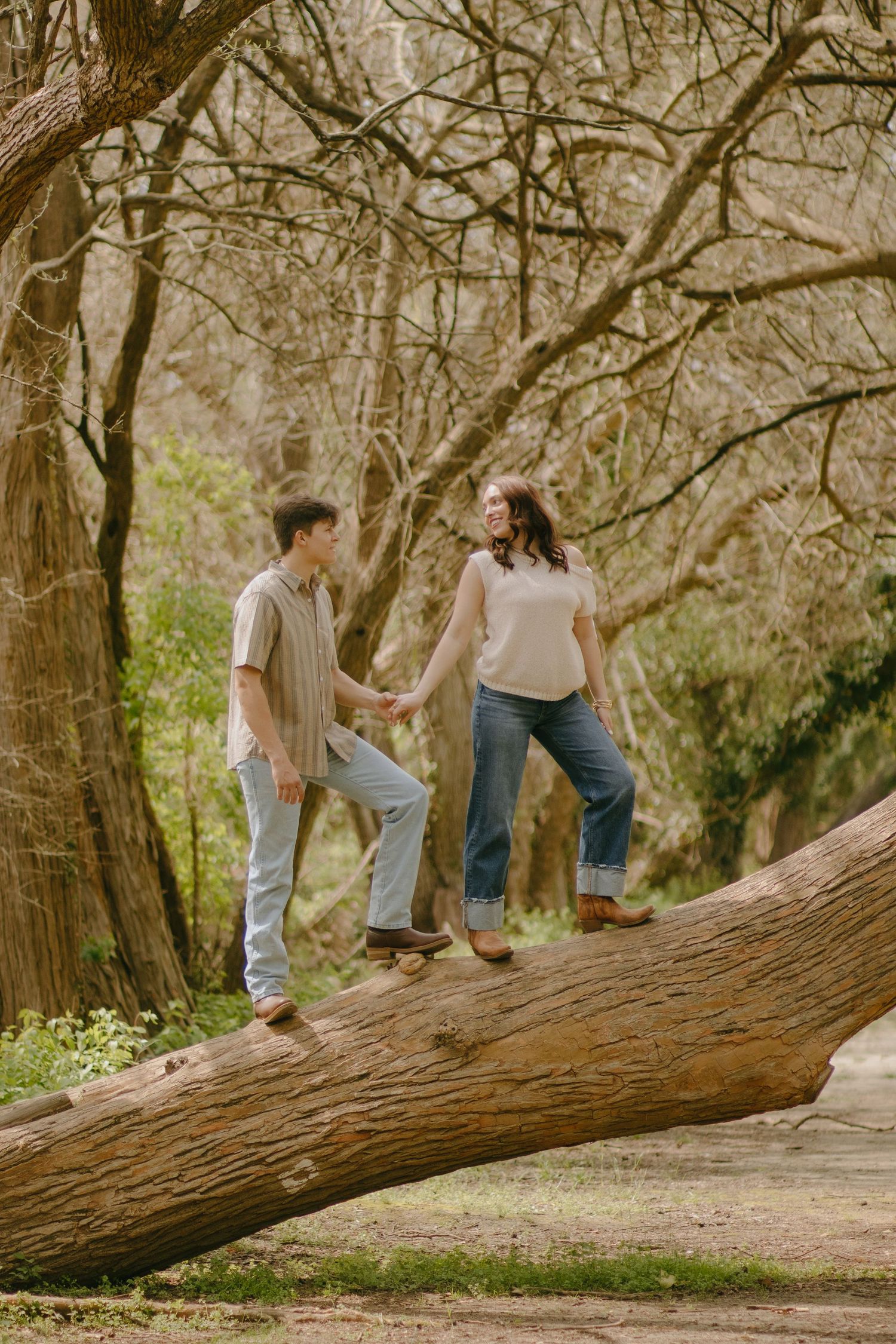 A couple sitting and talking on a fallen tree in a forest setting.