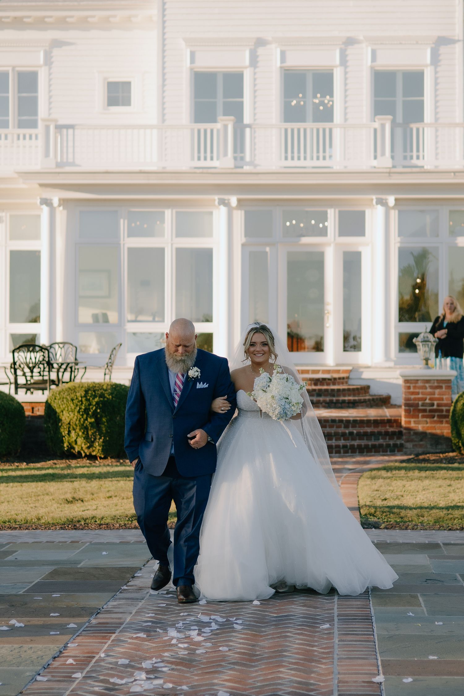 Wedding party walking along brick pathway outside white building.