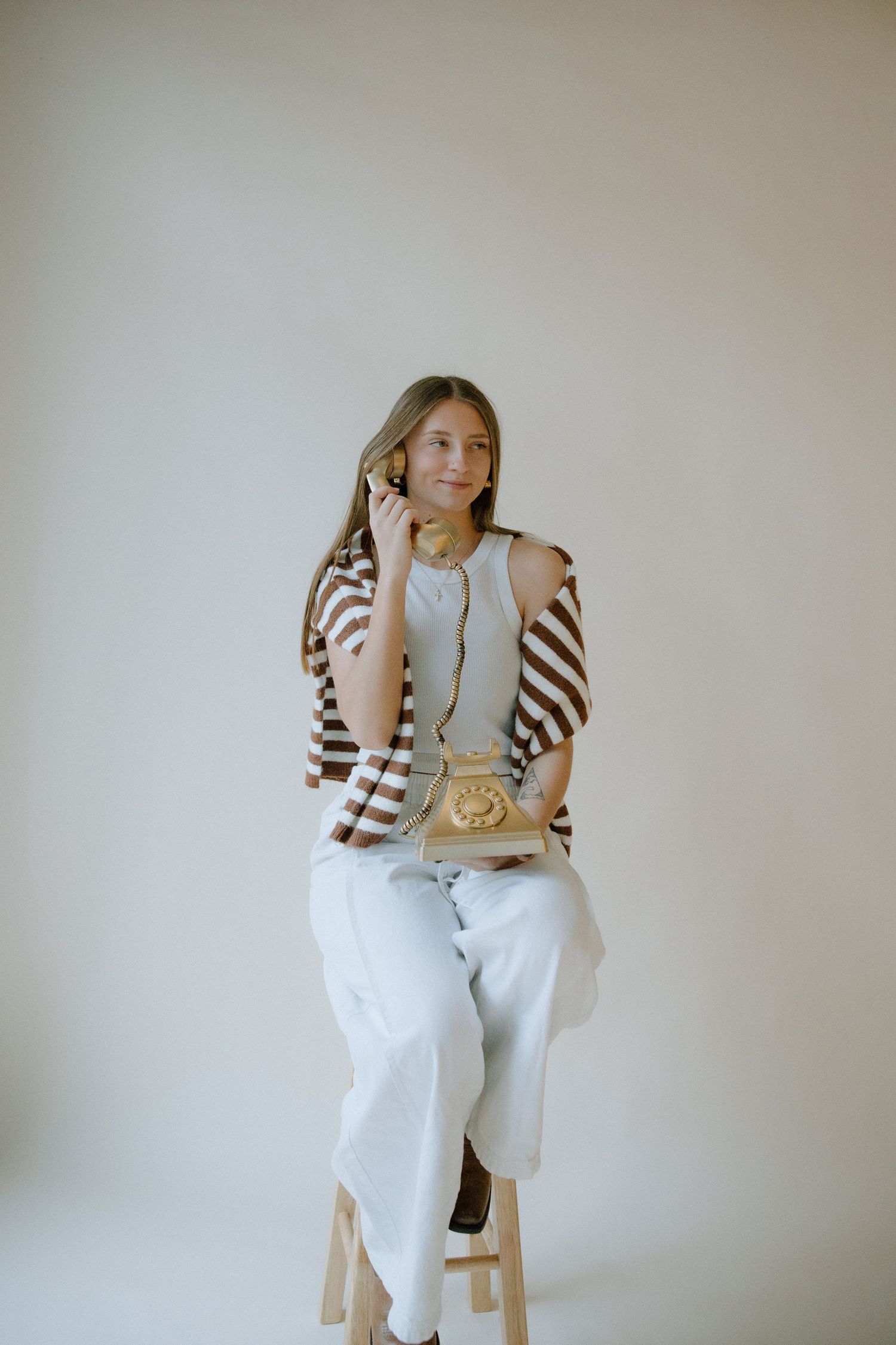 A figure in white clothing sits on a wooden stool against a neutral wall in a minimalist photo series.