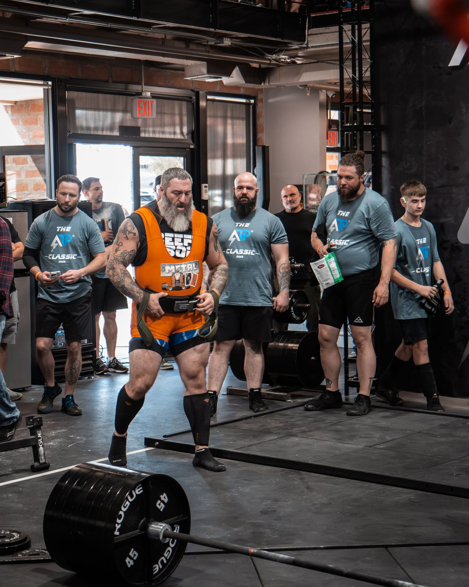 Athletes performing deadlifts with heavy barbells during an intense competition event at a CrossFit-style gym.
