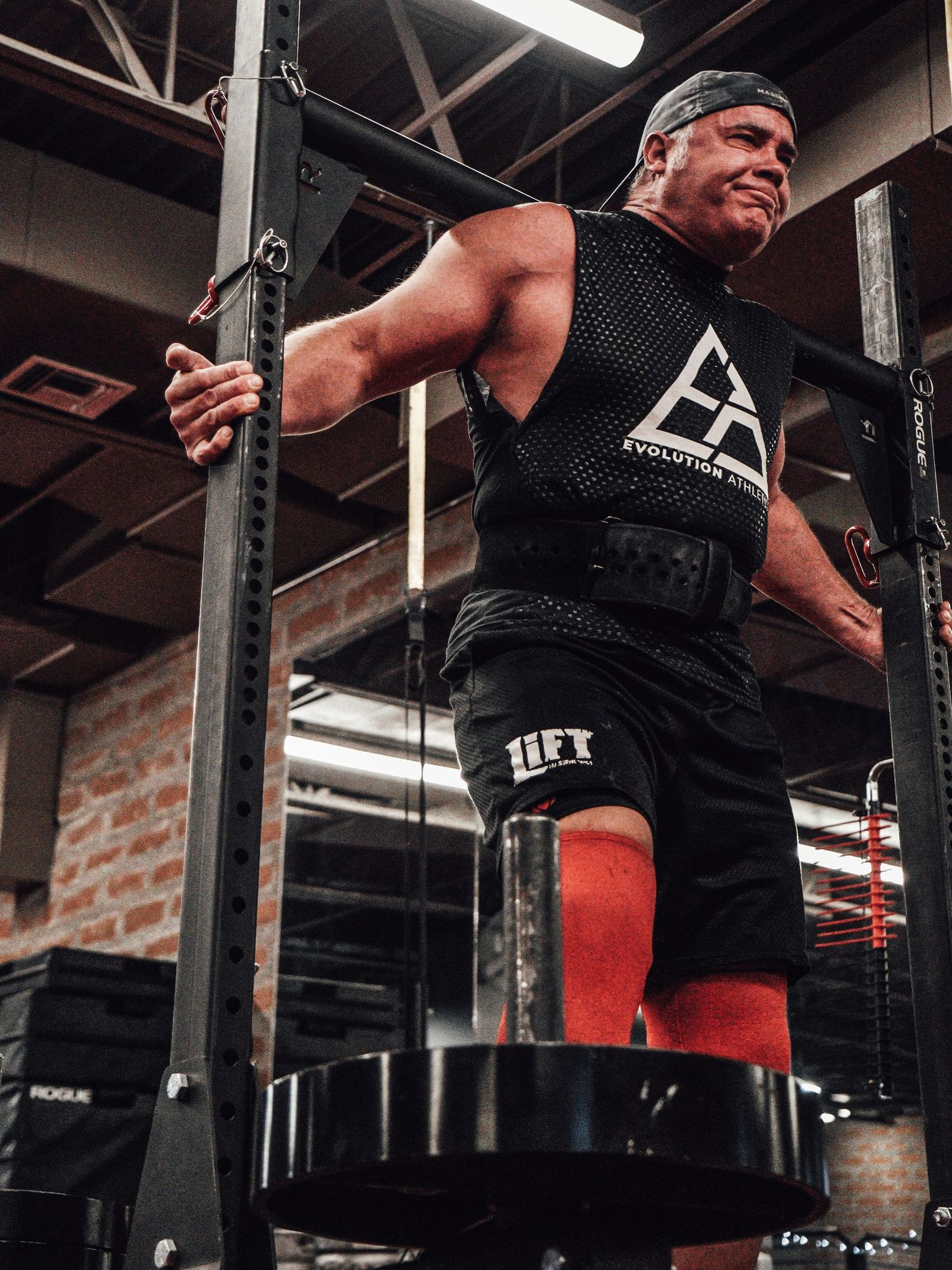 Person in black workout gear using weight training equipment in industrial gym space.