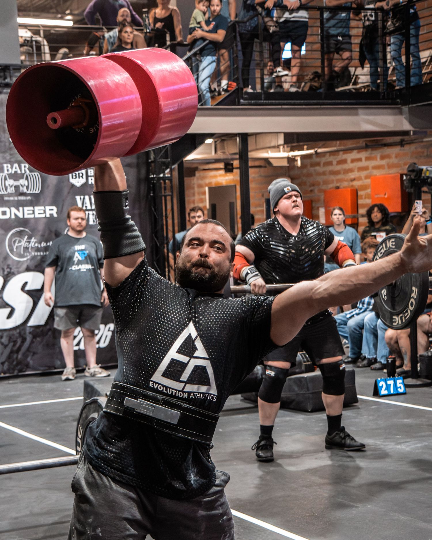 Competitors performing synchronized deadlifts with pink barbell sleeves during a strength competition.